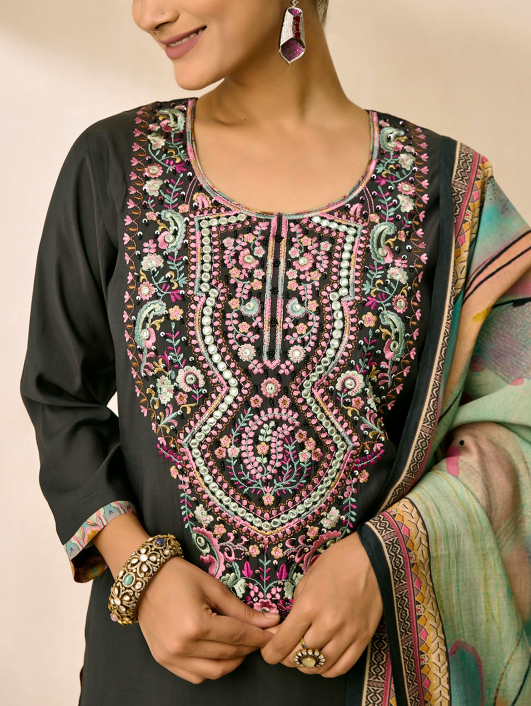 Woman wearing a black kurta with intricate floral embroidery on a beige background