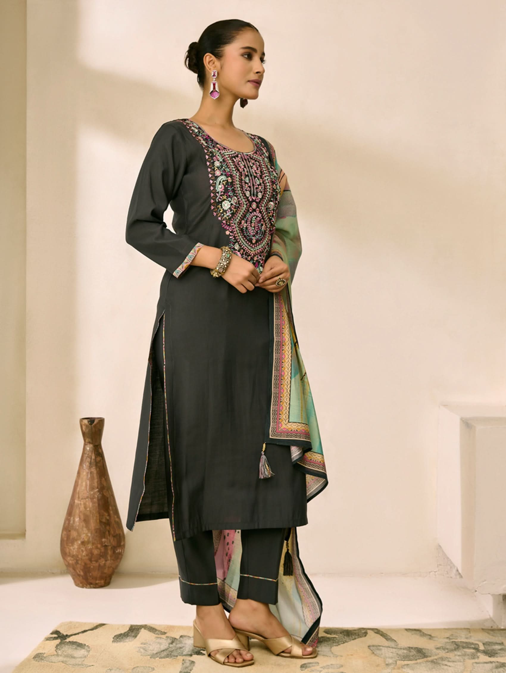 Woman in traditional outfit with embroidered top and black pants, standing indoors.