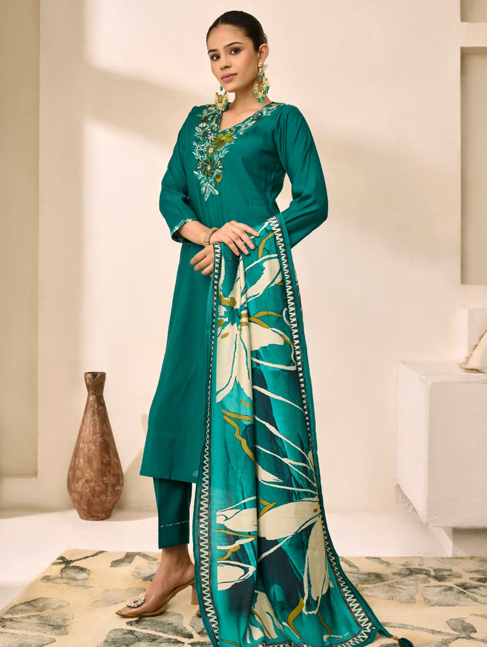 Woman wearing a teal traditional outfit with a floral scarf in a minimalistic setting