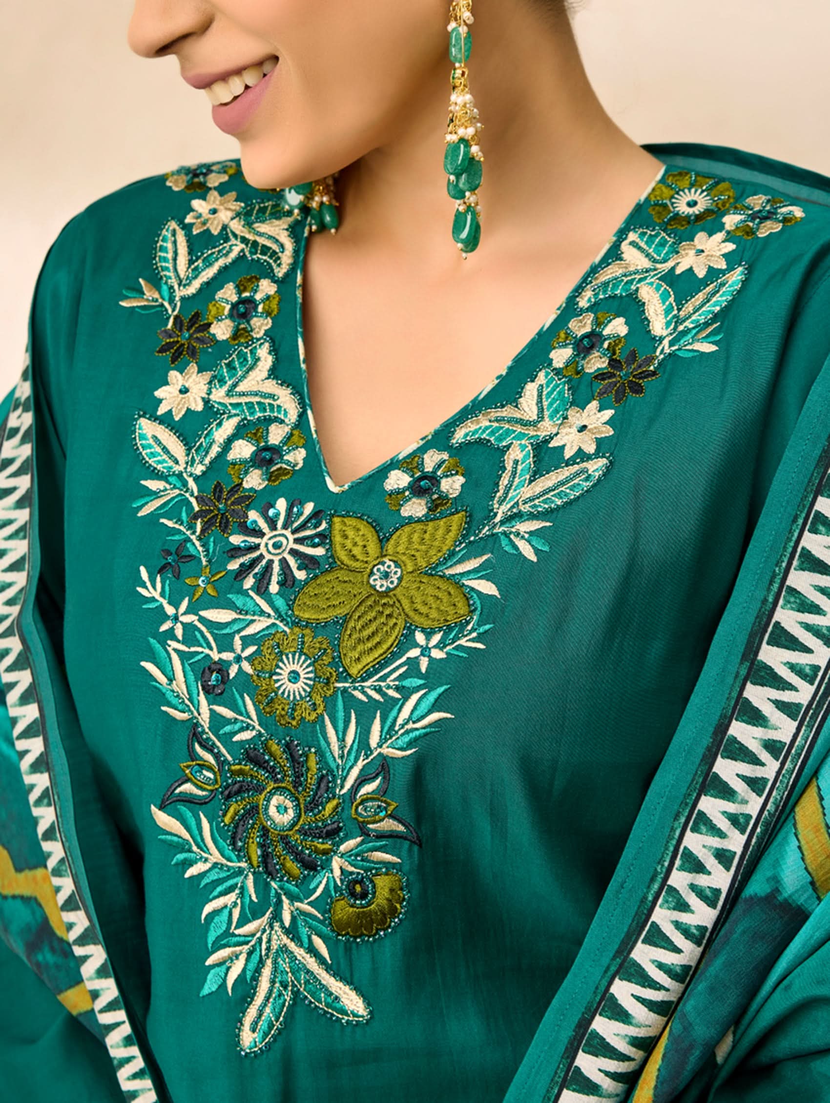 Teal embroidered garment with floral patterns on a beige background
