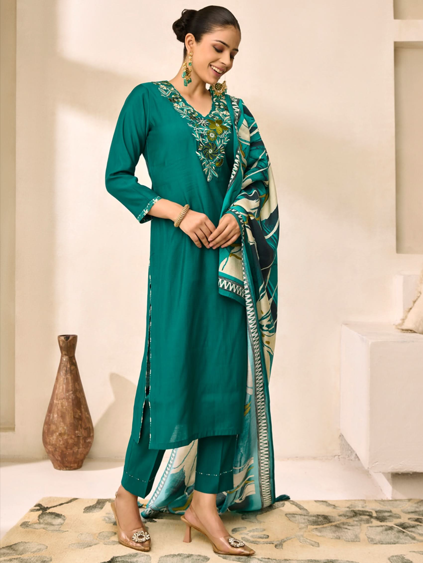 Woman wearing a teal traditional outfit with a matching dupatta in a minimalistic room.