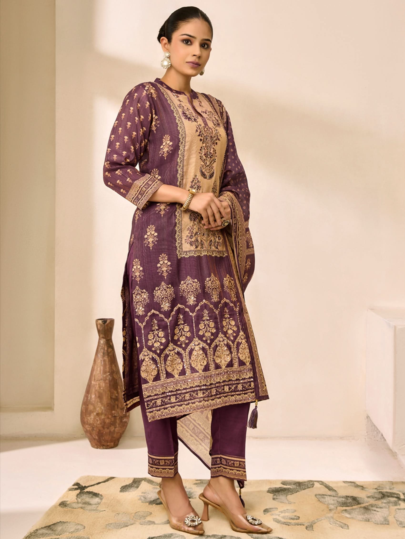 Woman wearing a traditional outfit with purple and gold patterns in a minimalistic setting.