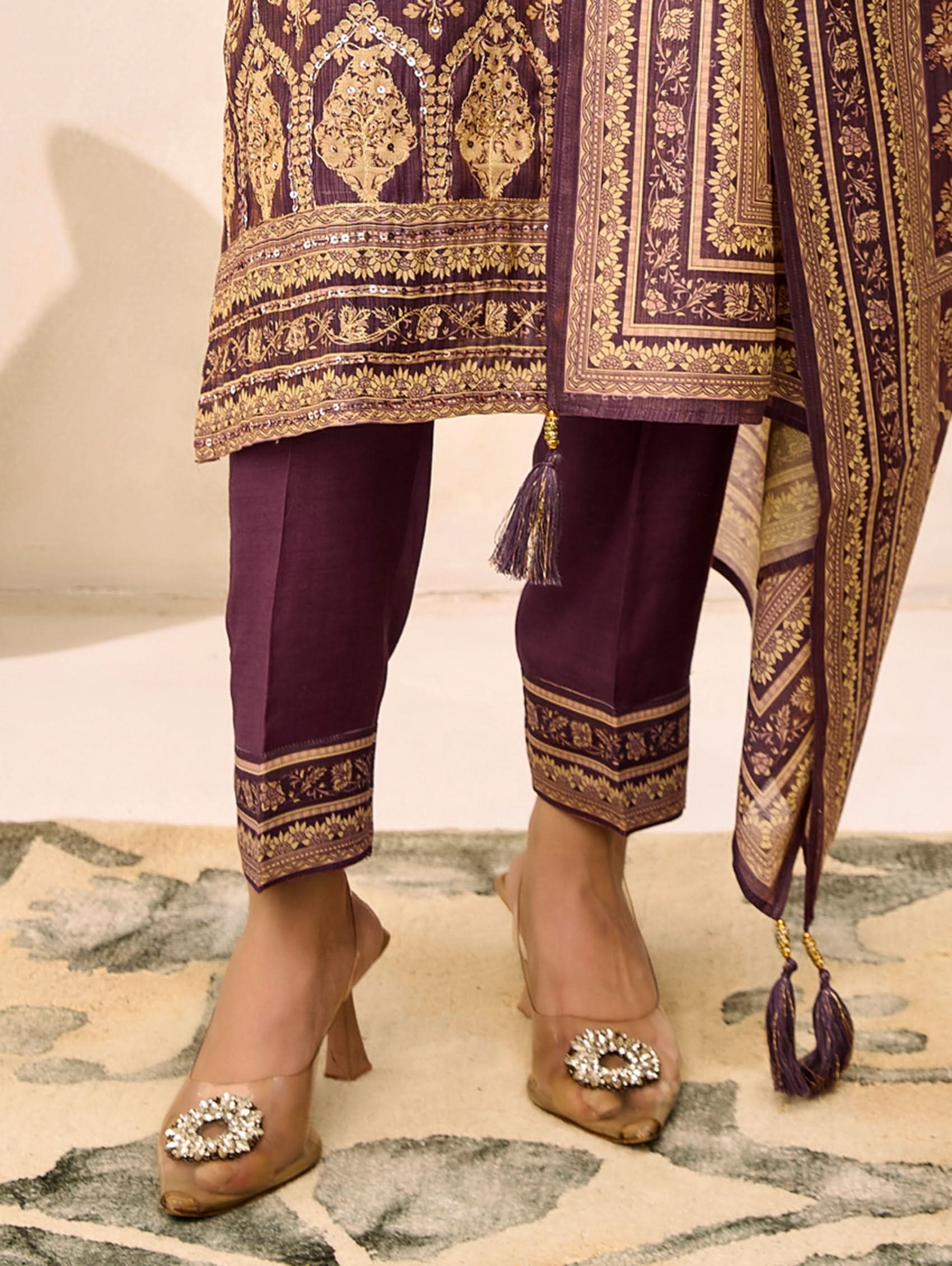 Purple traditional outfit with gold embroidery, matching pants, and high-heeled shoes on a patterned rug.