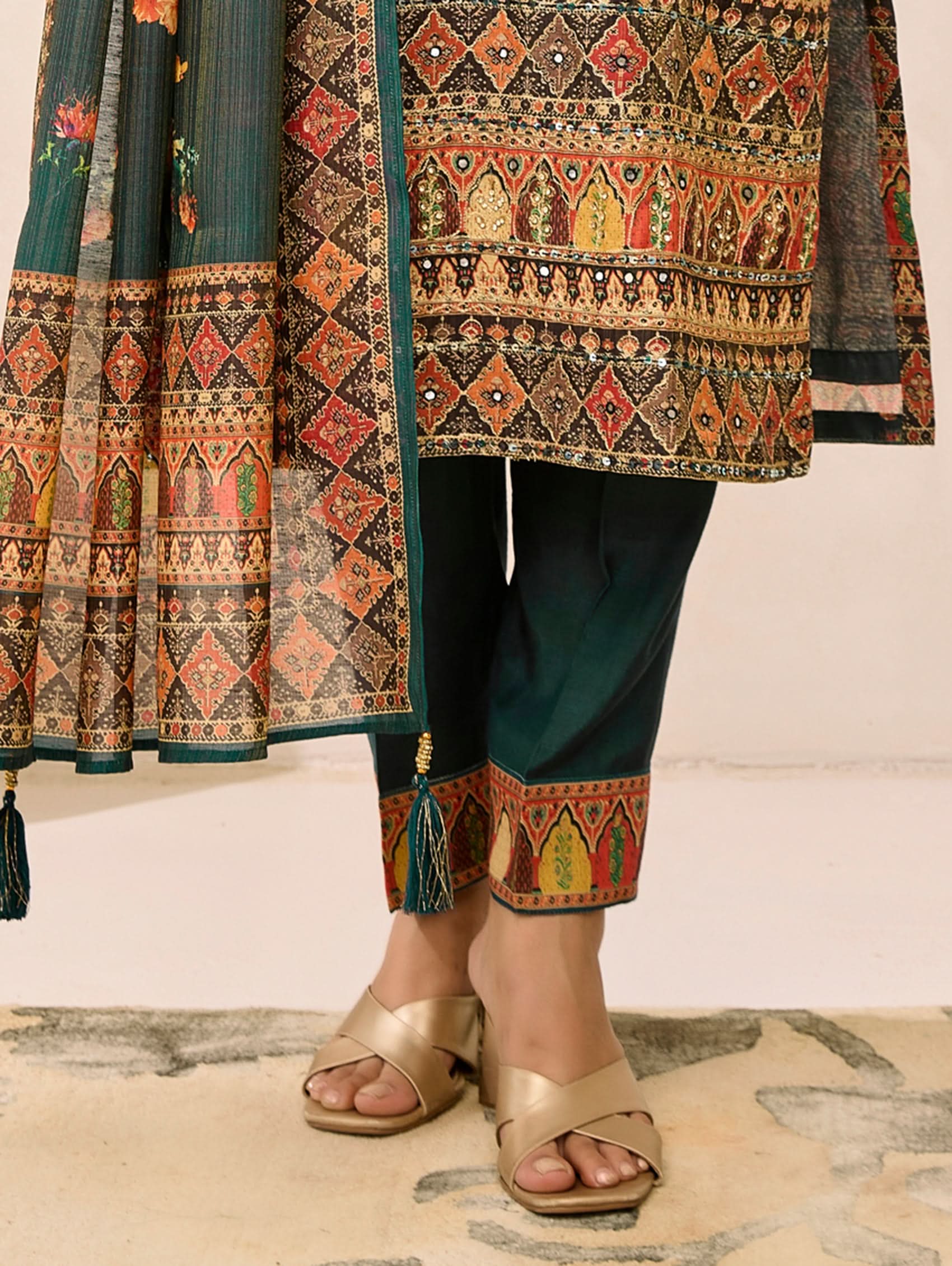 Traditional outfit with a patterned top and black pants, paired with gold sandals on a light background.