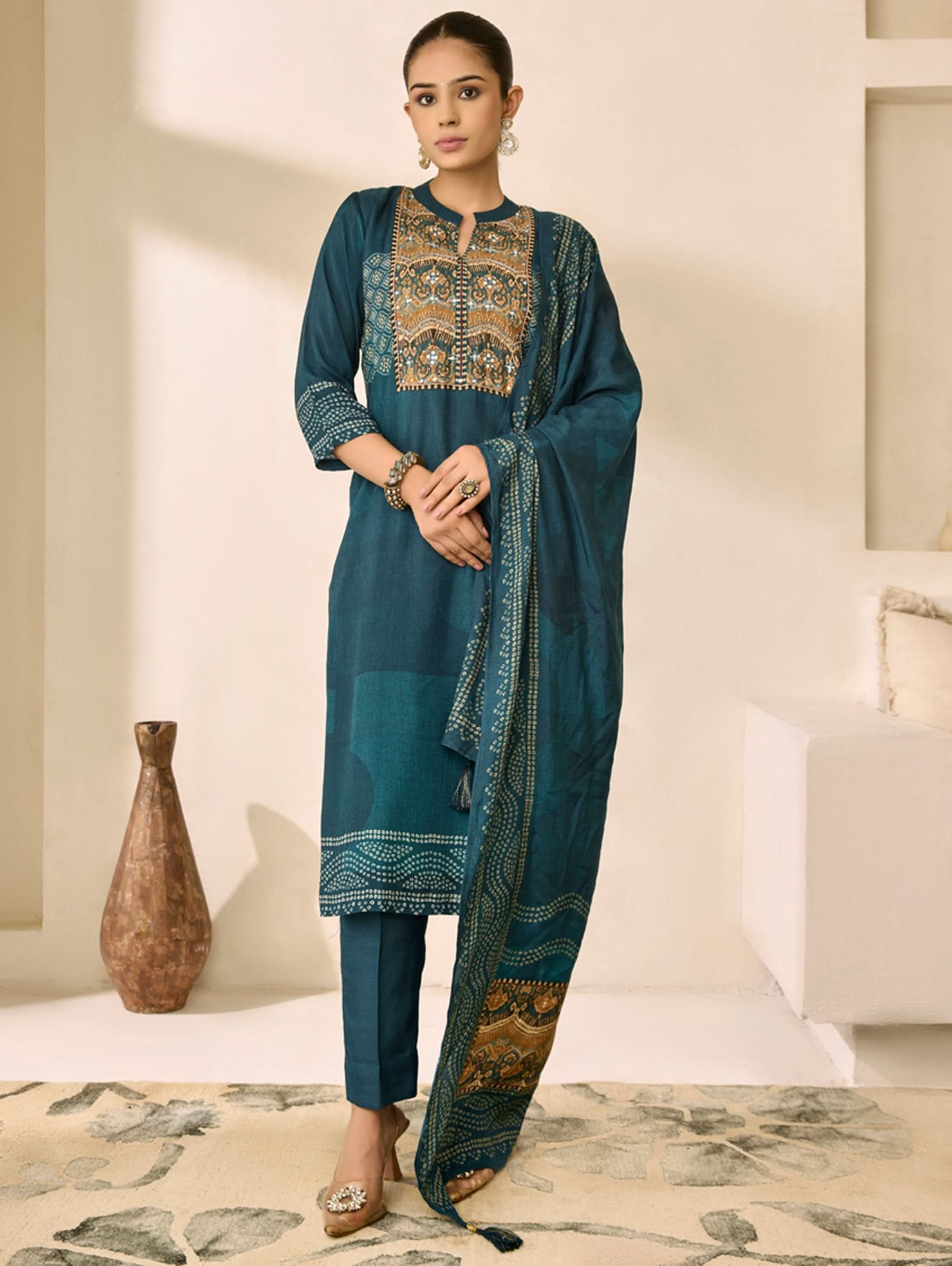 Woman wearing a blue embroidered traditional outfit in a minimalistic room.