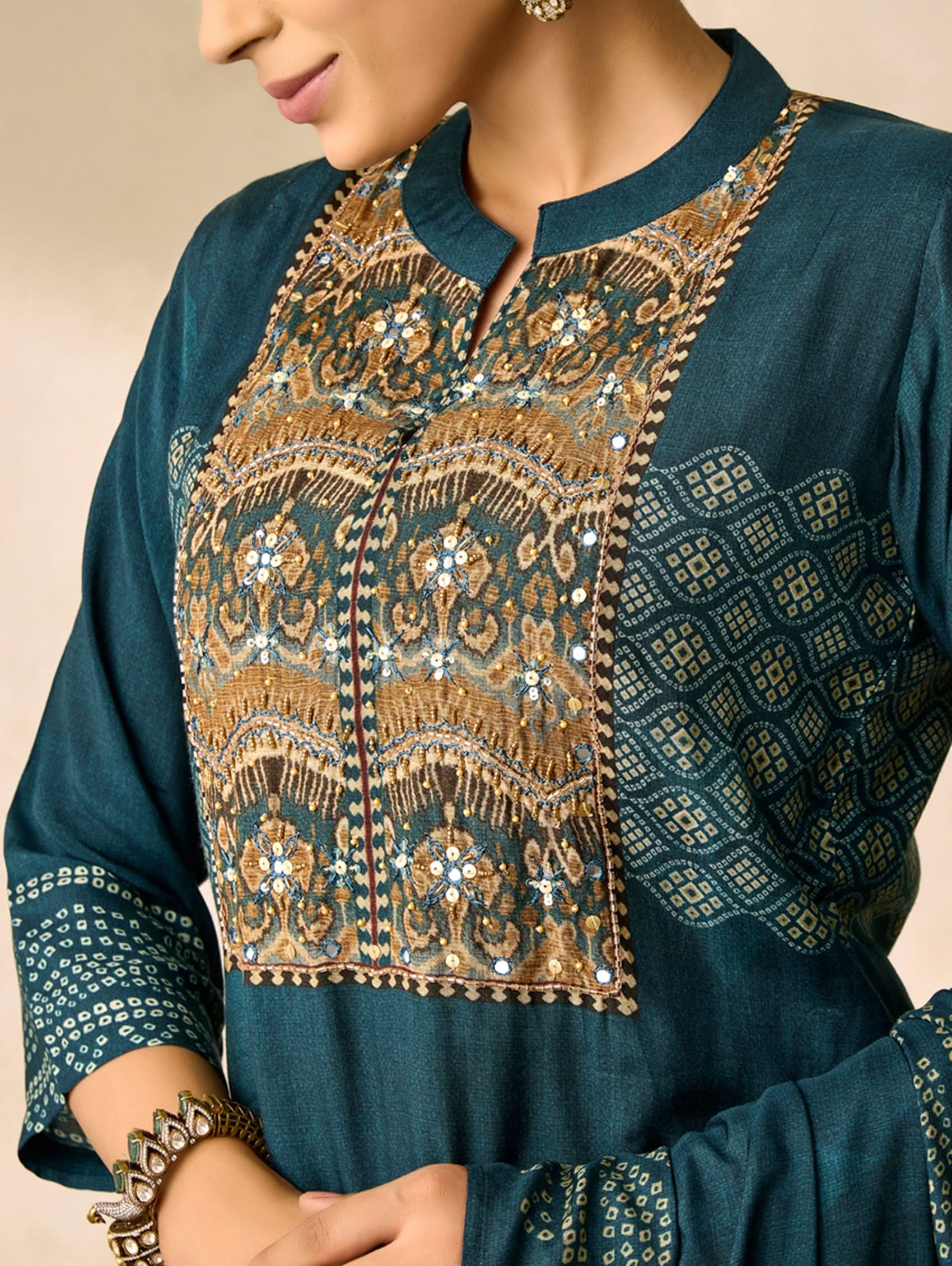 Teal embroidered top with gold details on a beige background