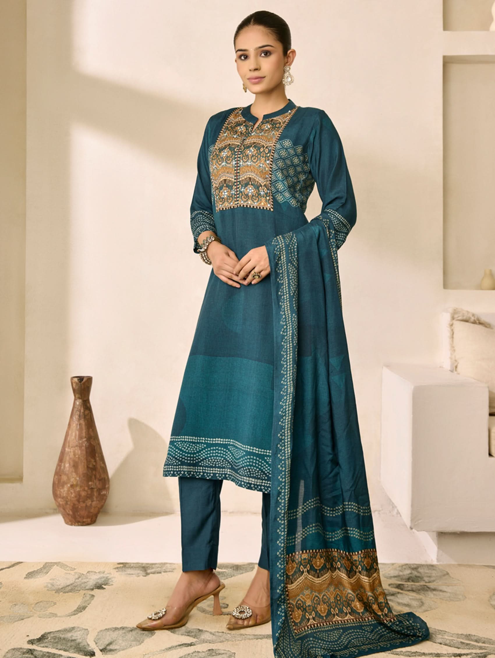 Woman wearing a teal embroidered traditional outfit in a minimalistic room.