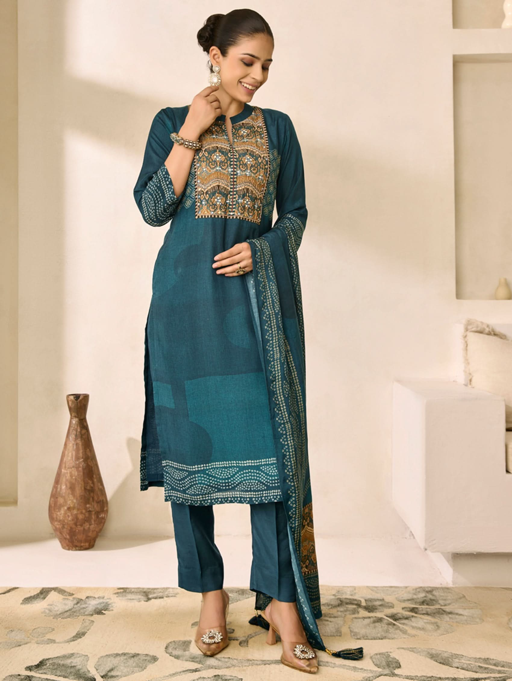 Woman wearing a teal traditional outfit with gold embroidery in a well-lit room.