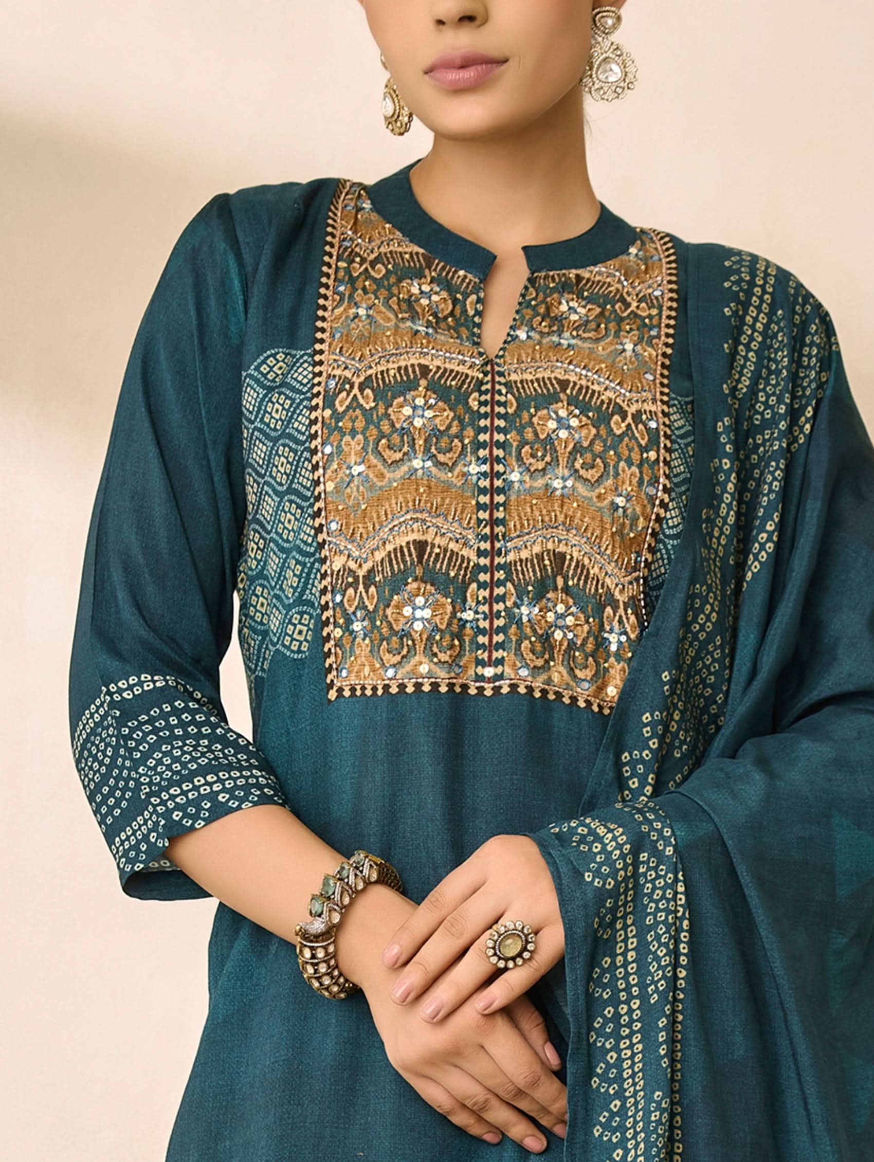 Teal traditional outfit with gold embroidery on a beige background