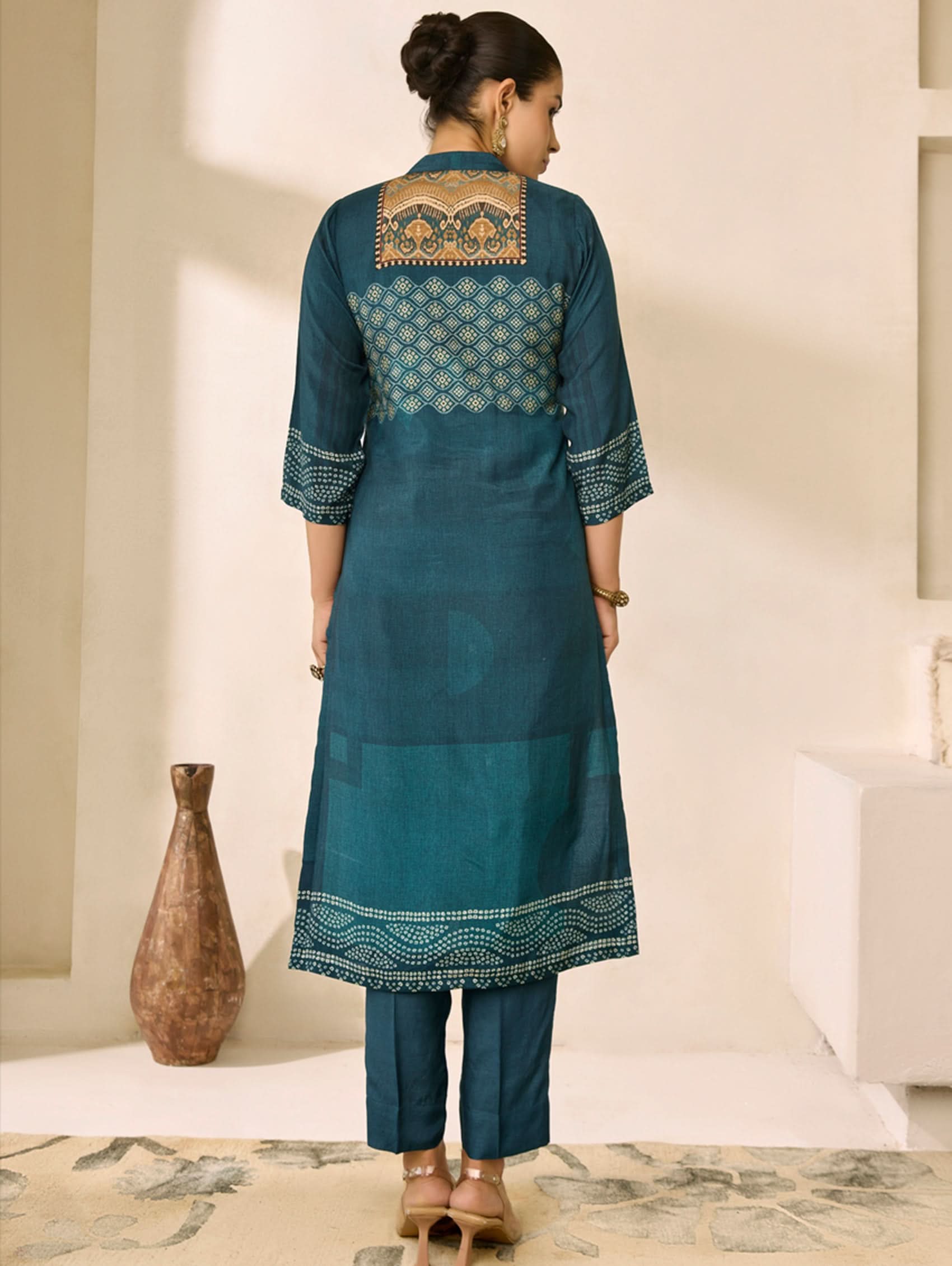 Woman wearing a blue embroidered traditional outfit in a minimalistic room.