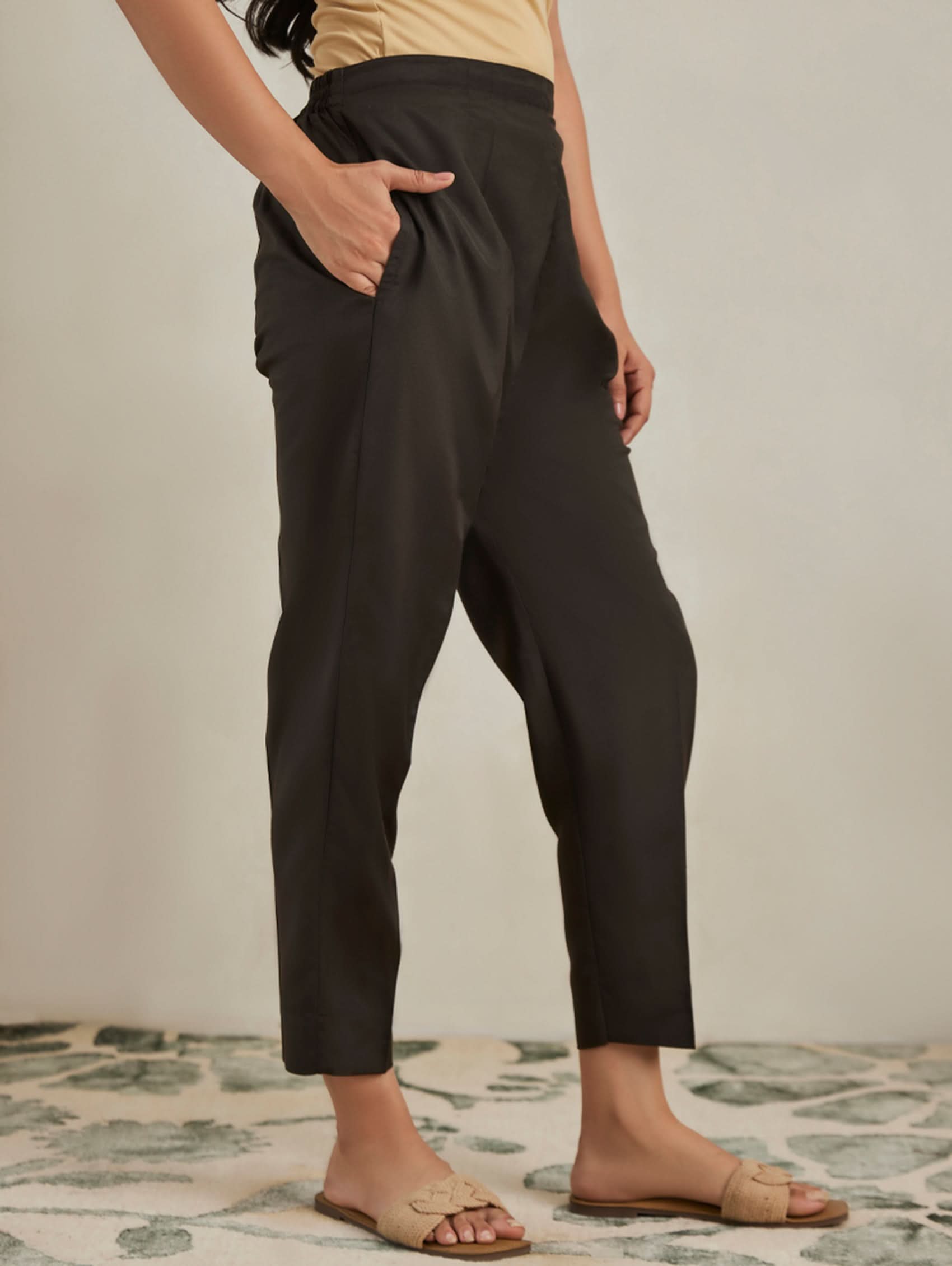 Person wearing black pants standing on a patterned rug with a neutral background