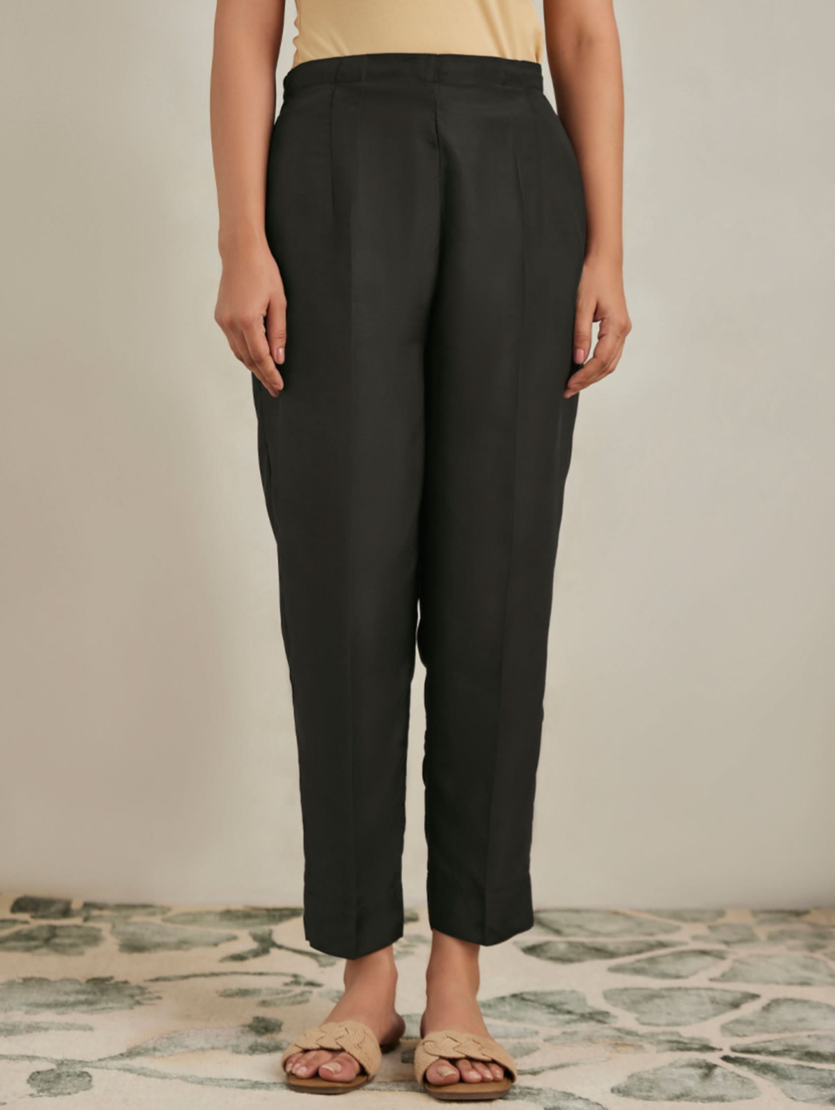 Person wearing black pants standing on a patterned floor with a neutral background