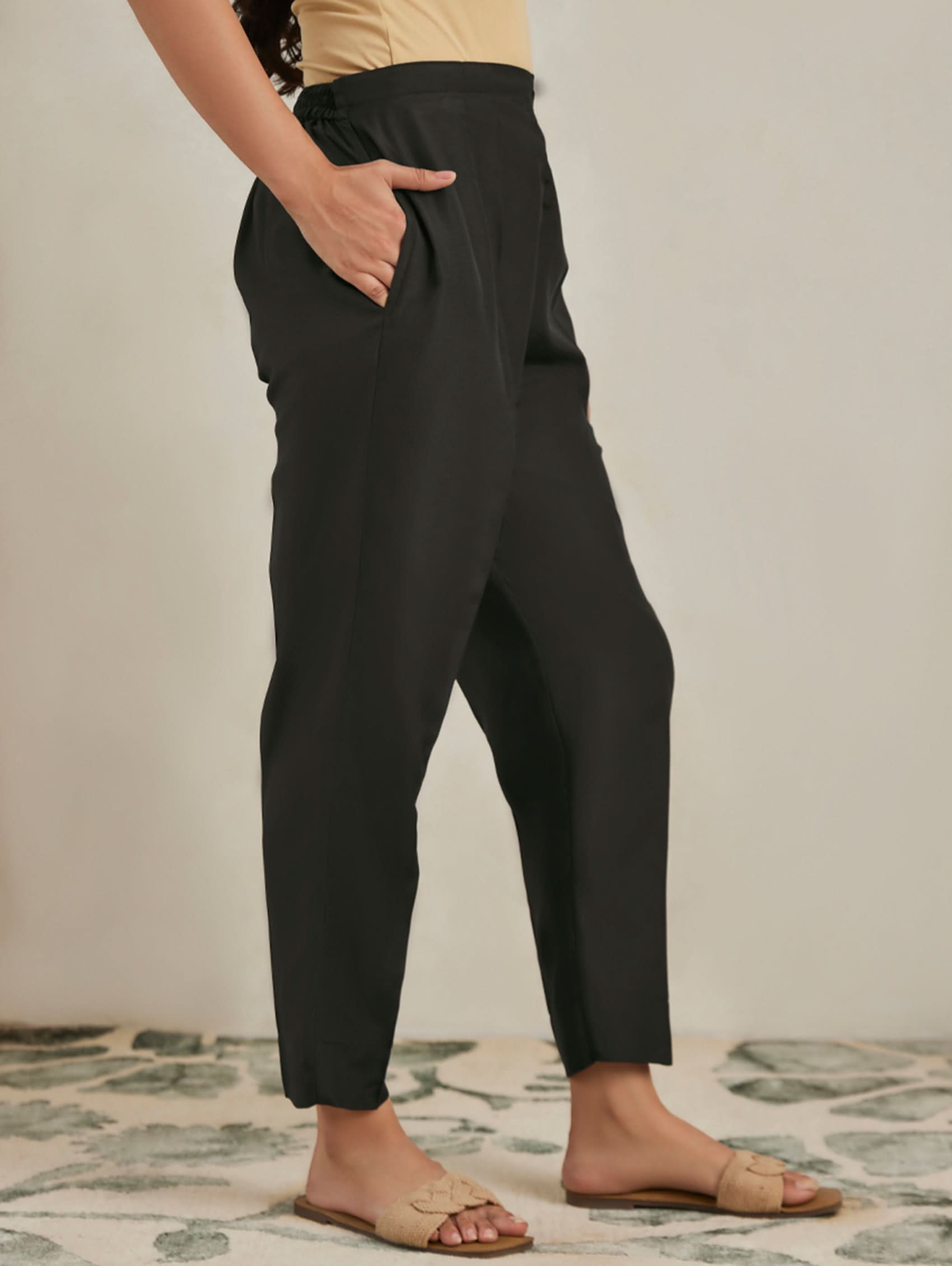 Person wearing black pants standing on a patterned rug with a neutral background