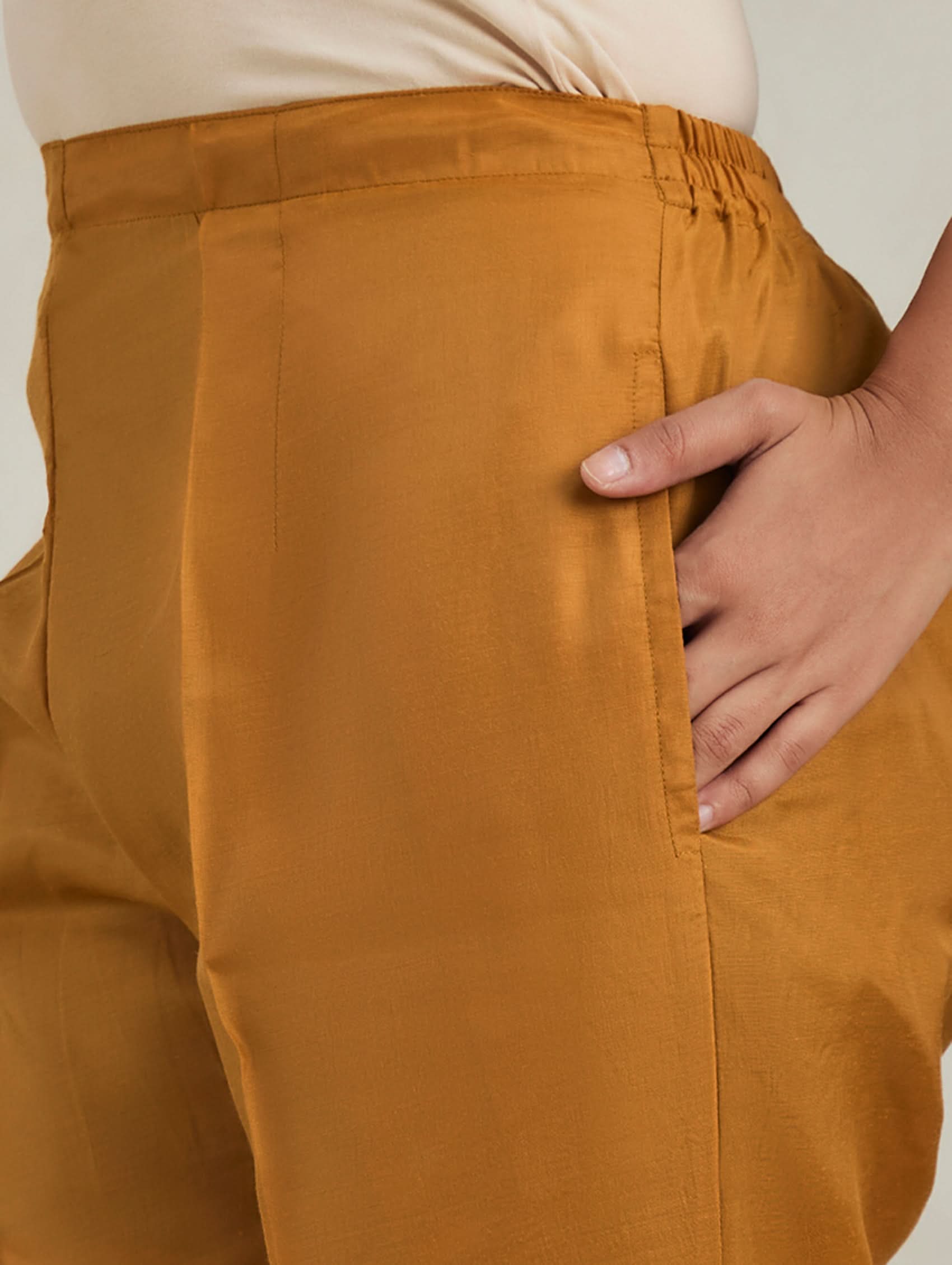 Brown pants with a hand touching the back pocket against a neutral background