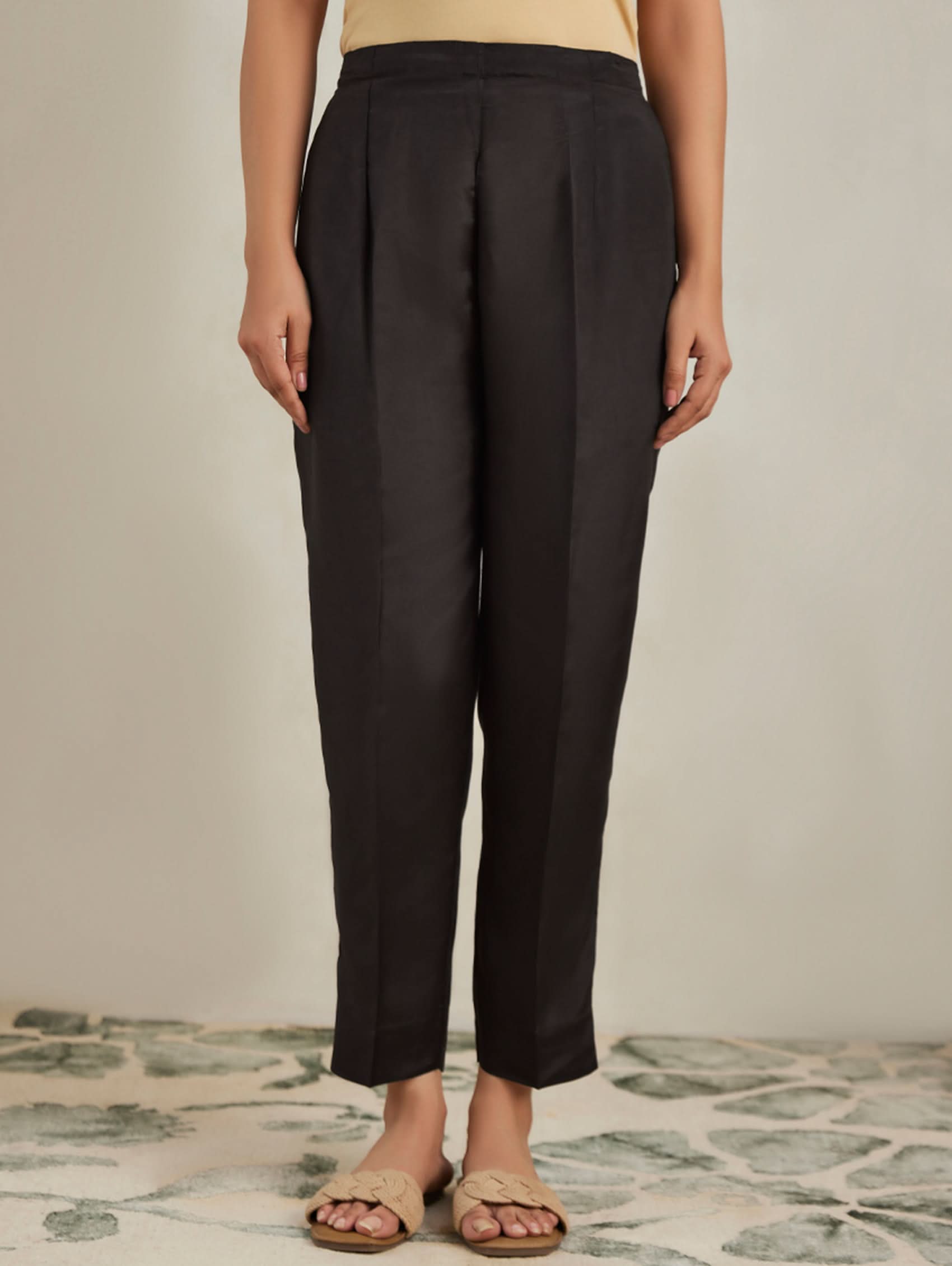 Person wearing black pants standing on a patterned floor with a neutral background