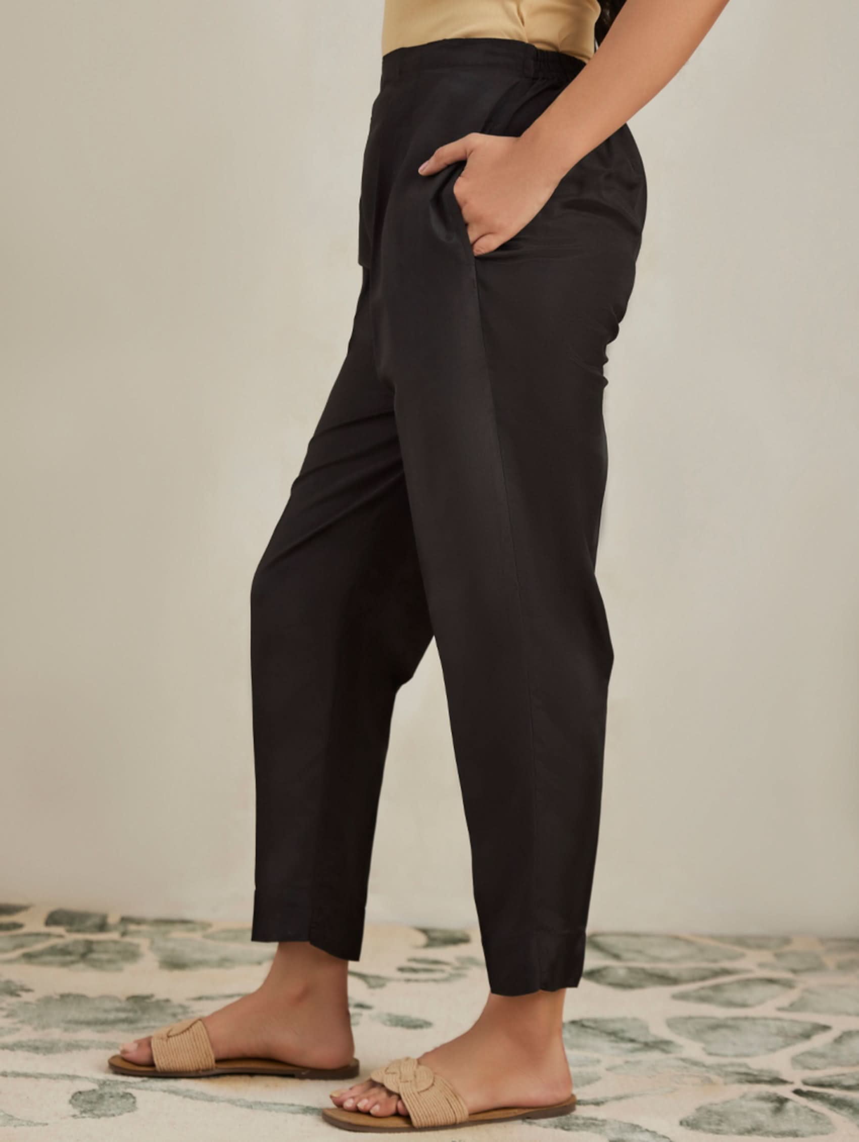 Person wearing black pants and beige sandals on a patterned floor.
