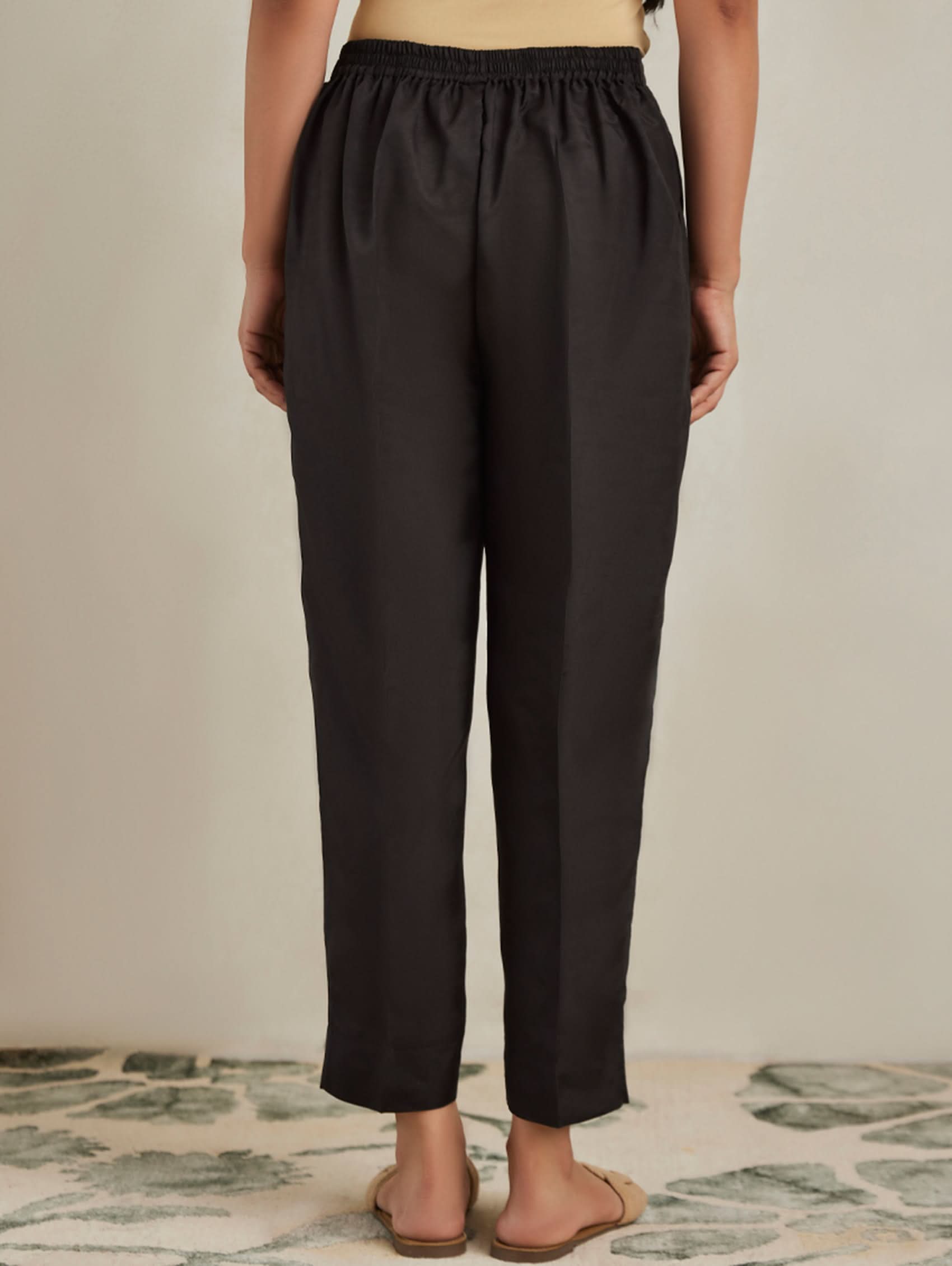 Person wearing black pants standing on a patterned rug with a neutral background