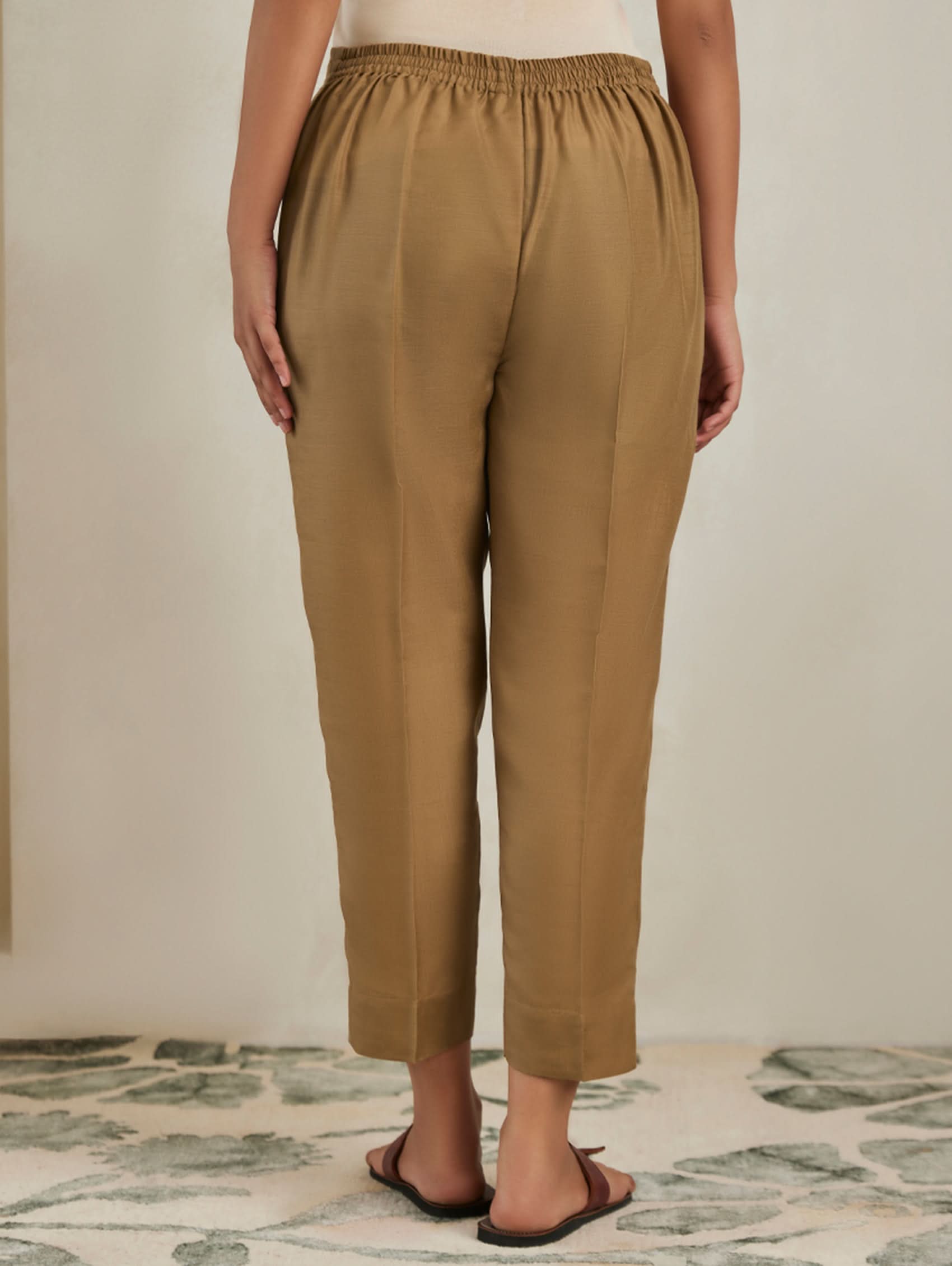Person wearing tan pants standing on a patterned rug with a neutral background