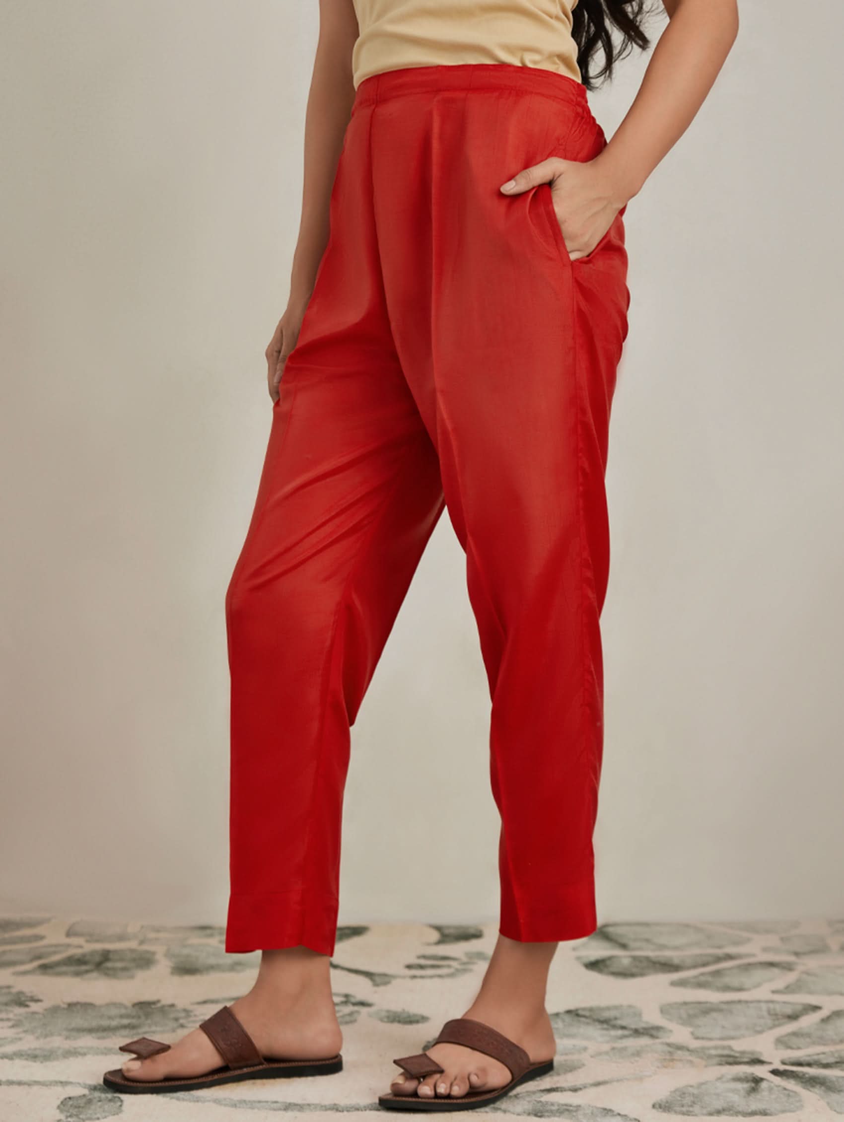 Person wearing red pants and brown sandals on a neutral background