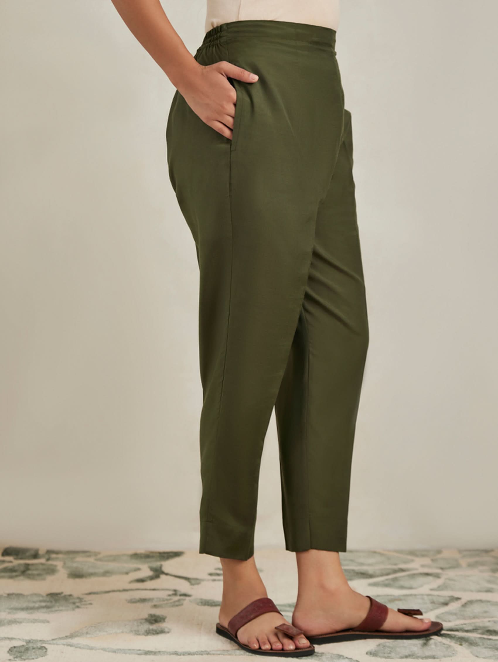 Person wearing olive green pants standing on a patterned rug with a neutral background
