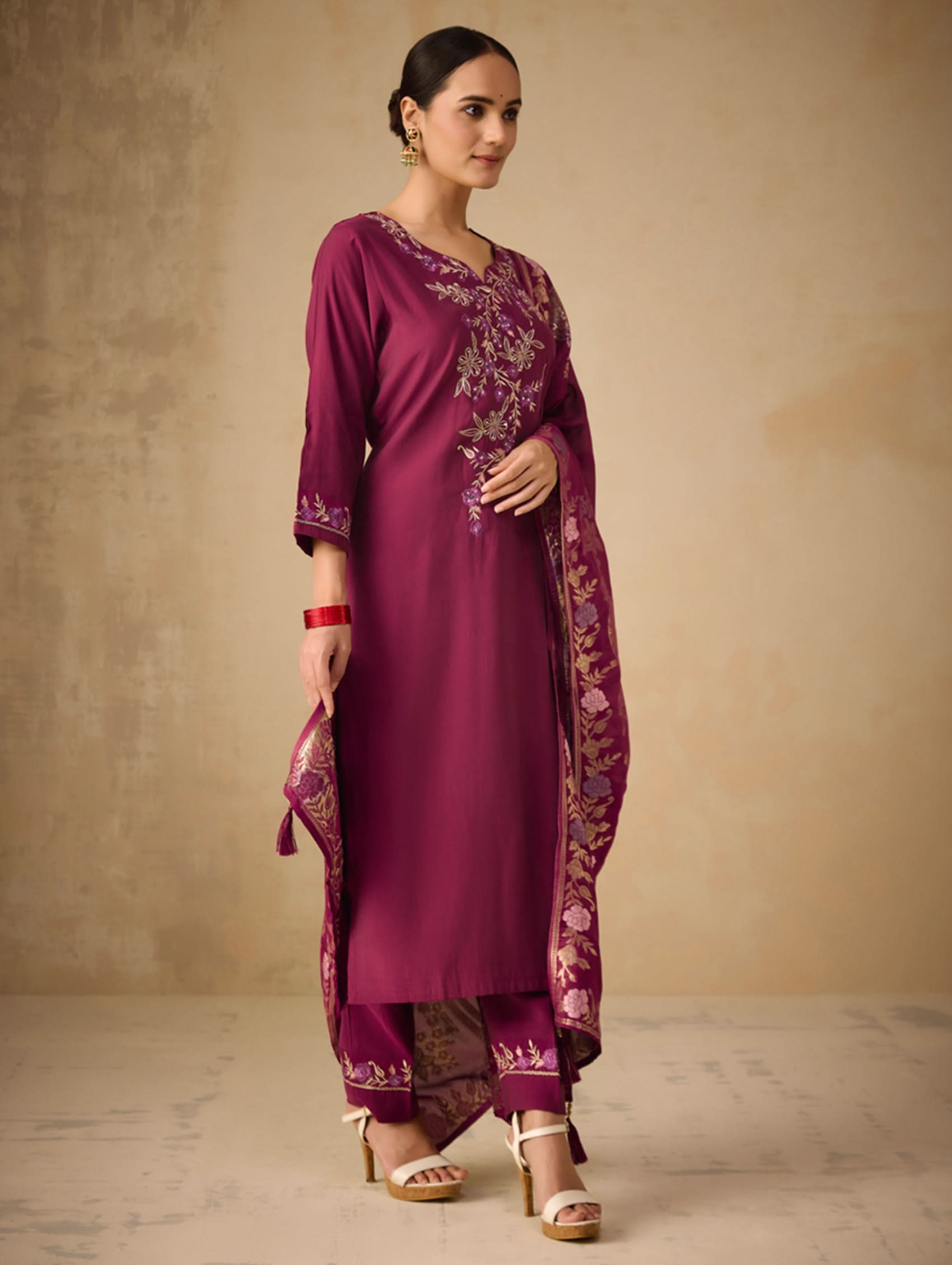 Woman wearing a purple embroidered traditional outfit against a beige background
