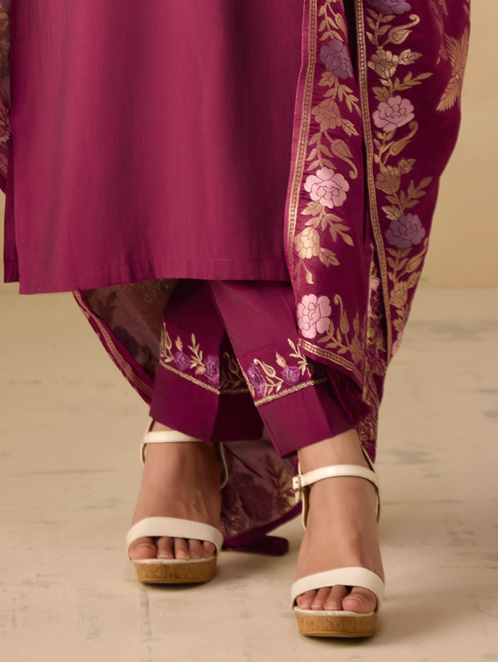 Purple traditional outfit with floral embroidery and white sandals on a neutral background