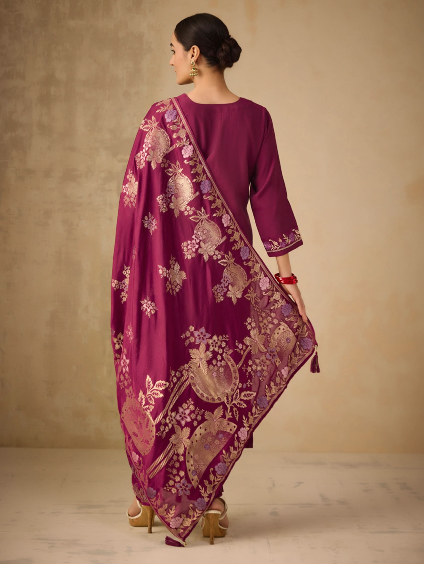Woman wearing a magenta traditional outfit with gold embroidery against a beige background