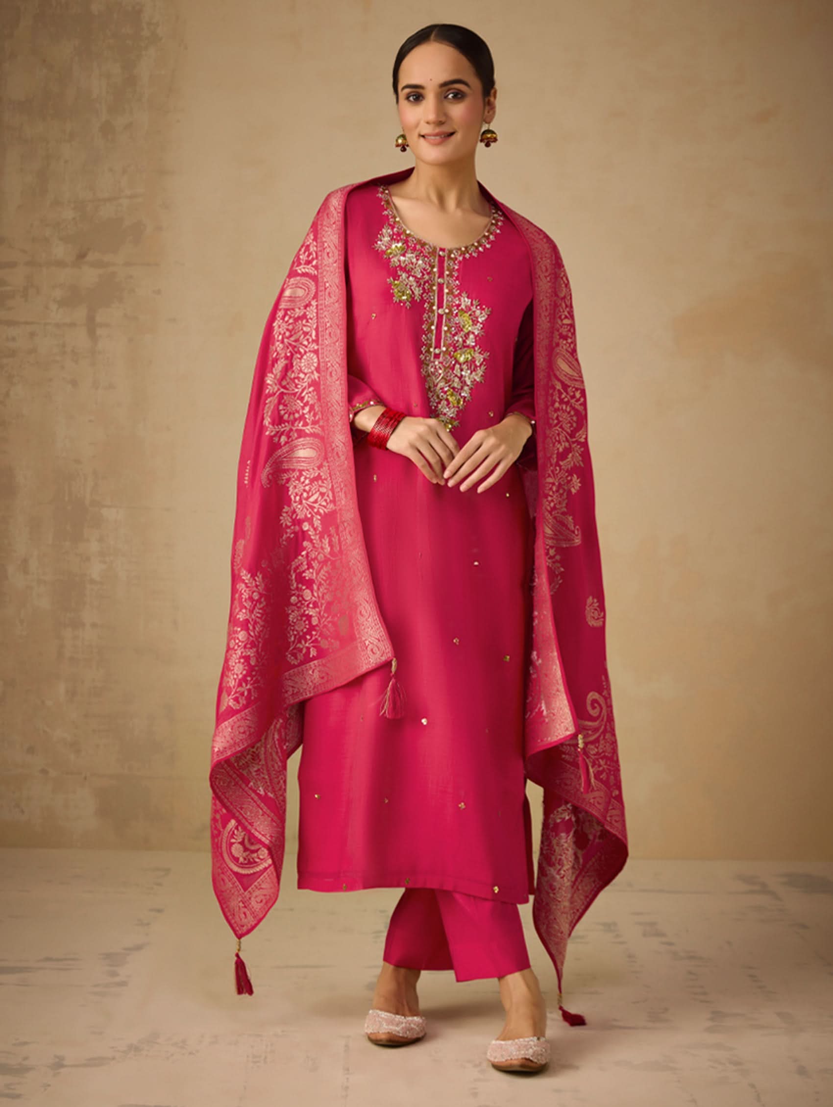 Woman wearing a pink traditional outfit with a matching dupatta on a beige background