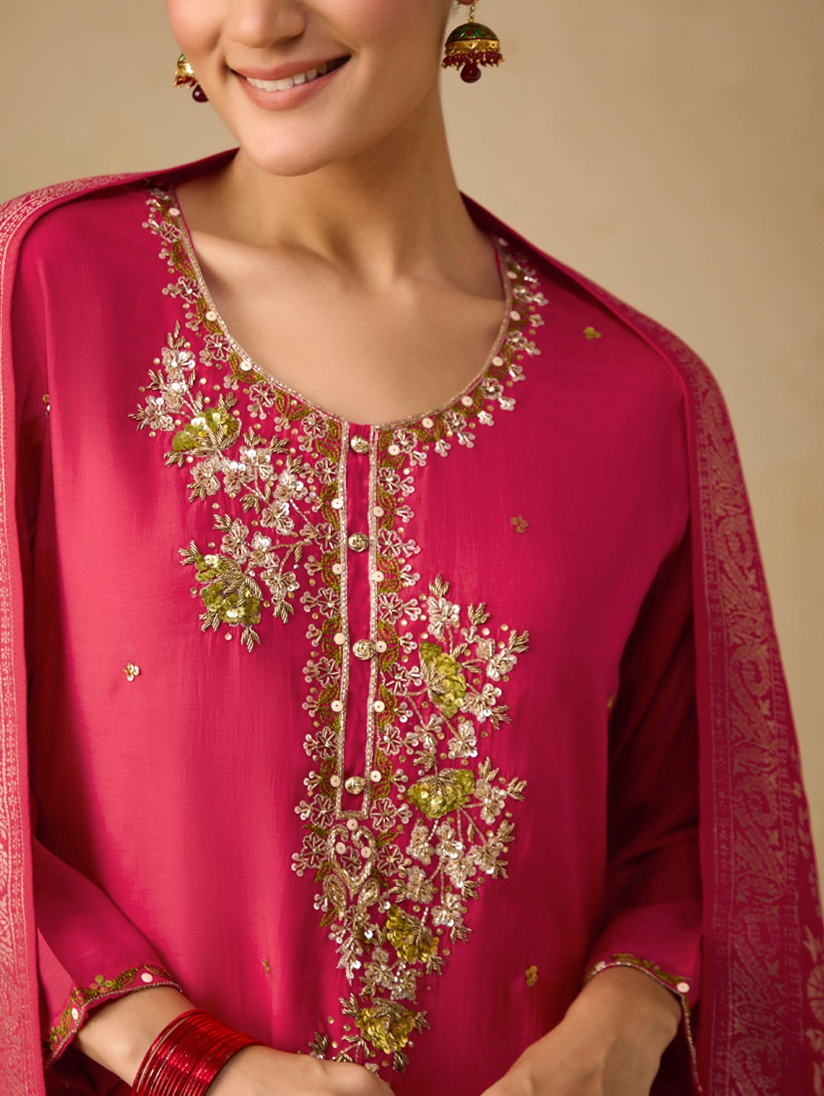 Woman wearing a pink embroidered traditional outfit with a beige background
