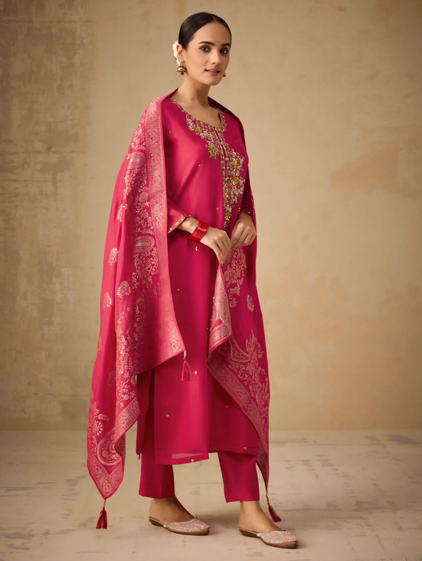 Woman wearing a pink traditional outfit with a matching dupatta against a beige background