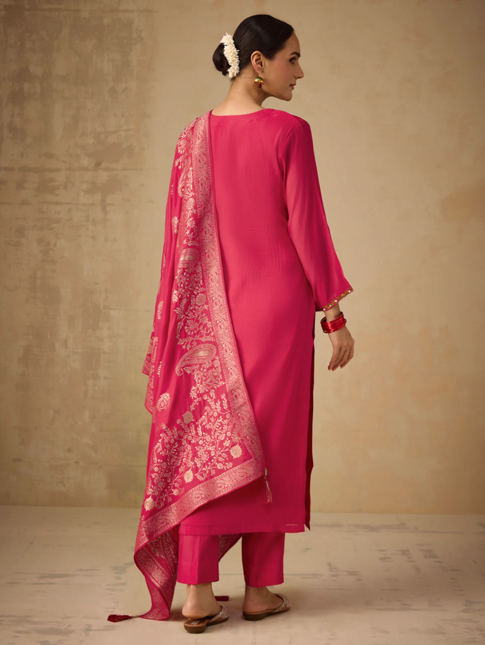 Woman wearing a bright pink traditional outfit with a matching dupatta against a beige background