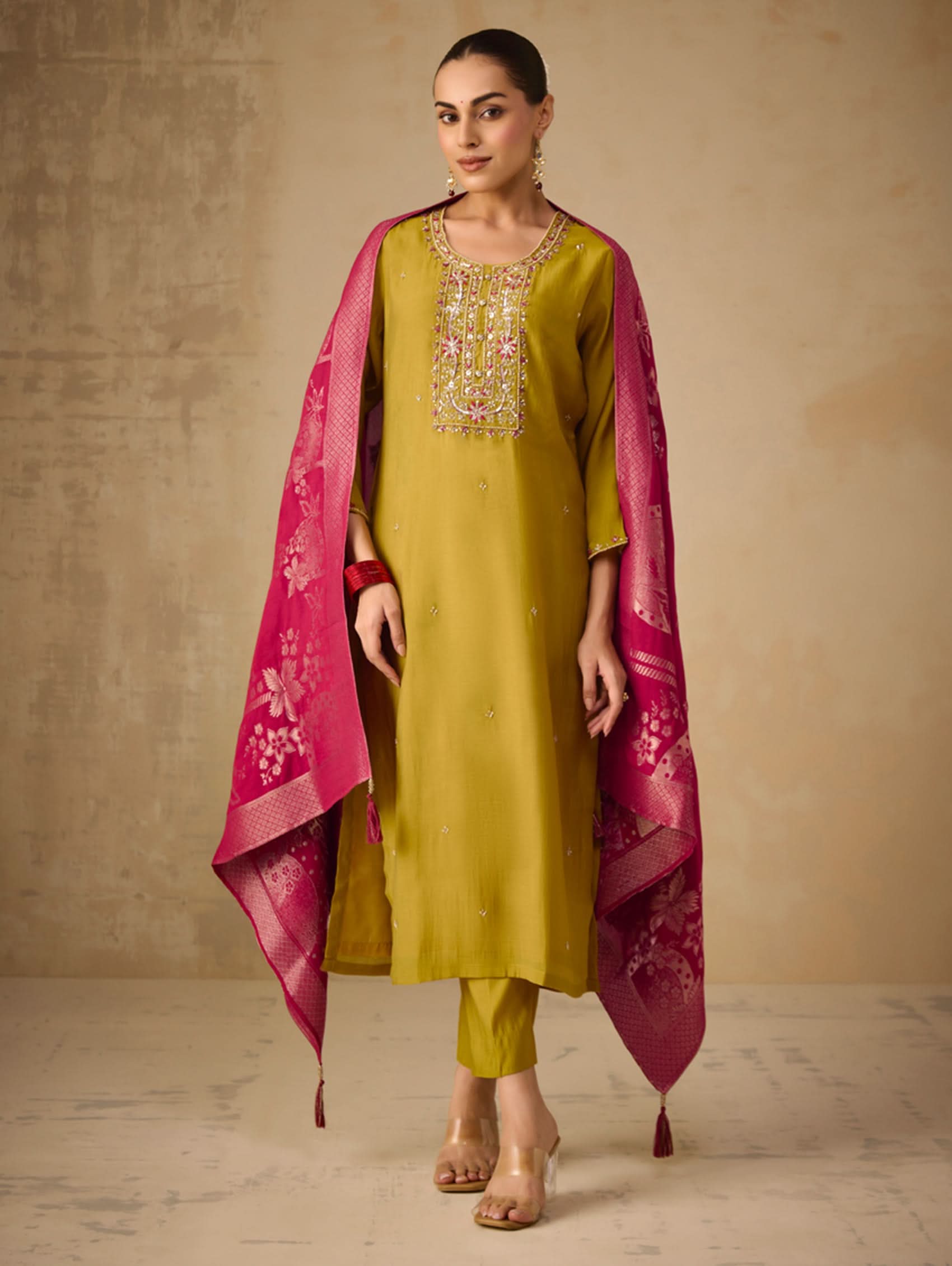 Woman wearing a green kurta with pink dupatta against a beige background