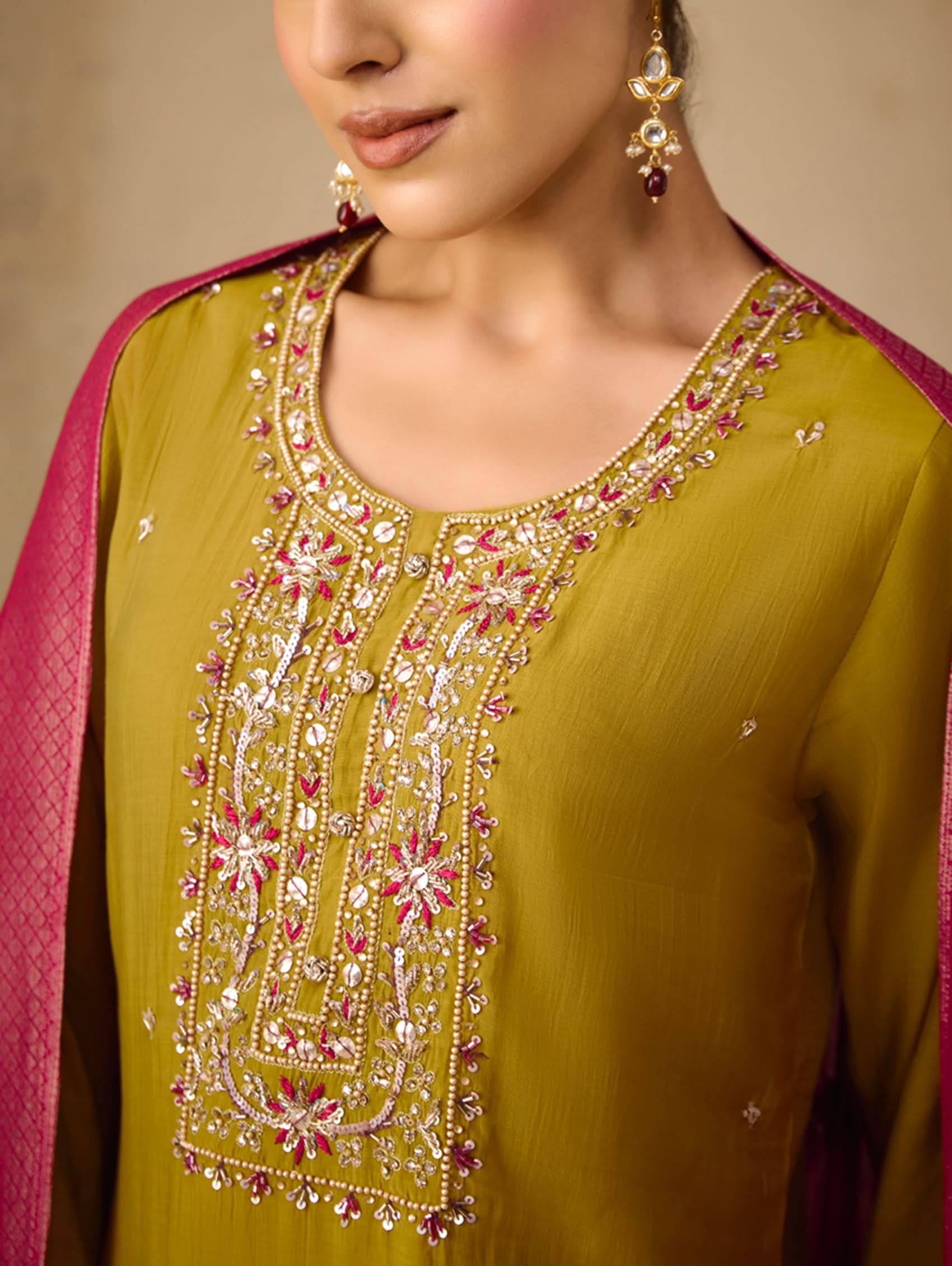 Close-up of a green embroidered garment with pink border and gold jewelry.