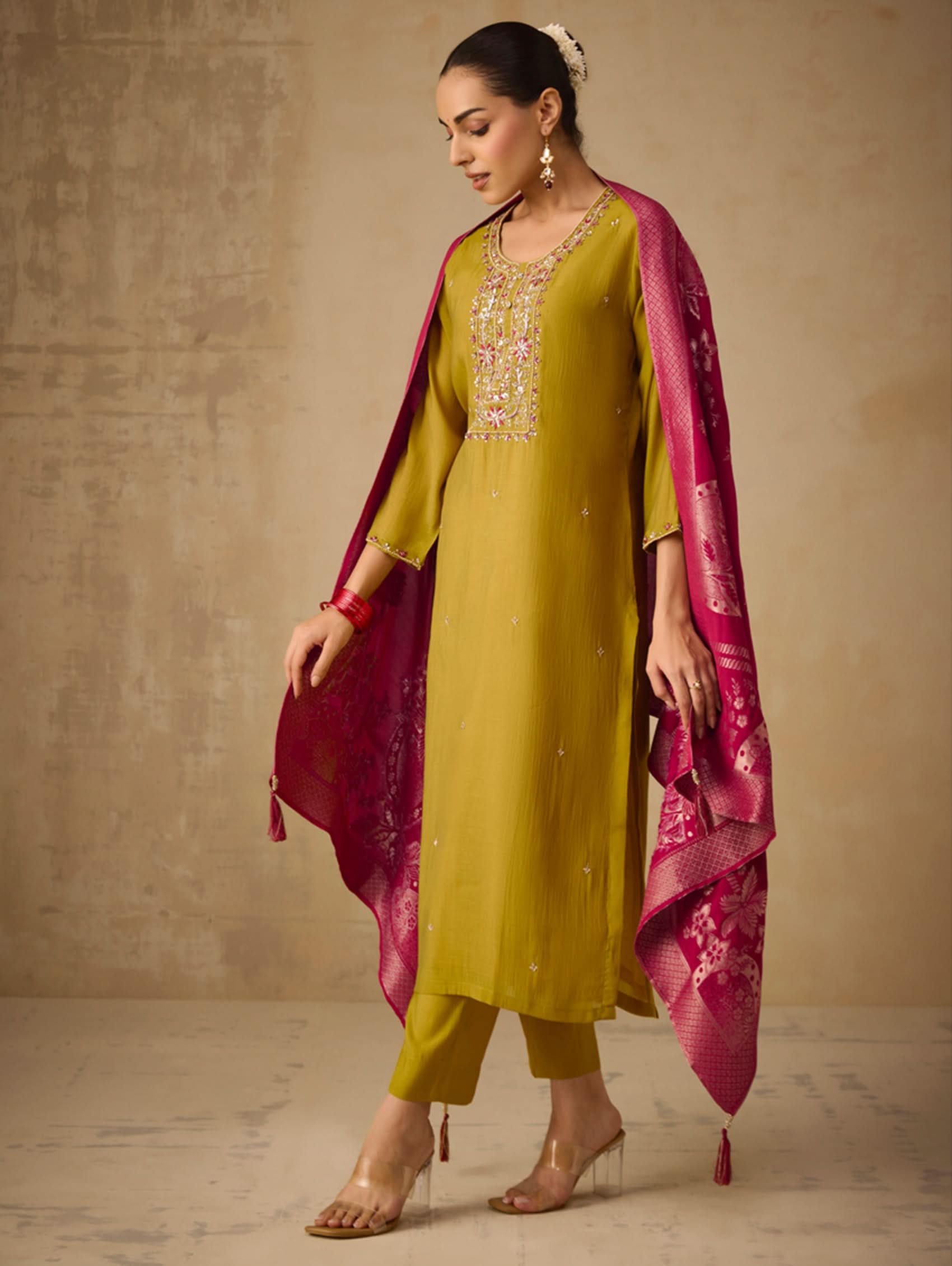 Woman wearing a green outfit with a pink dupatta against a beige background