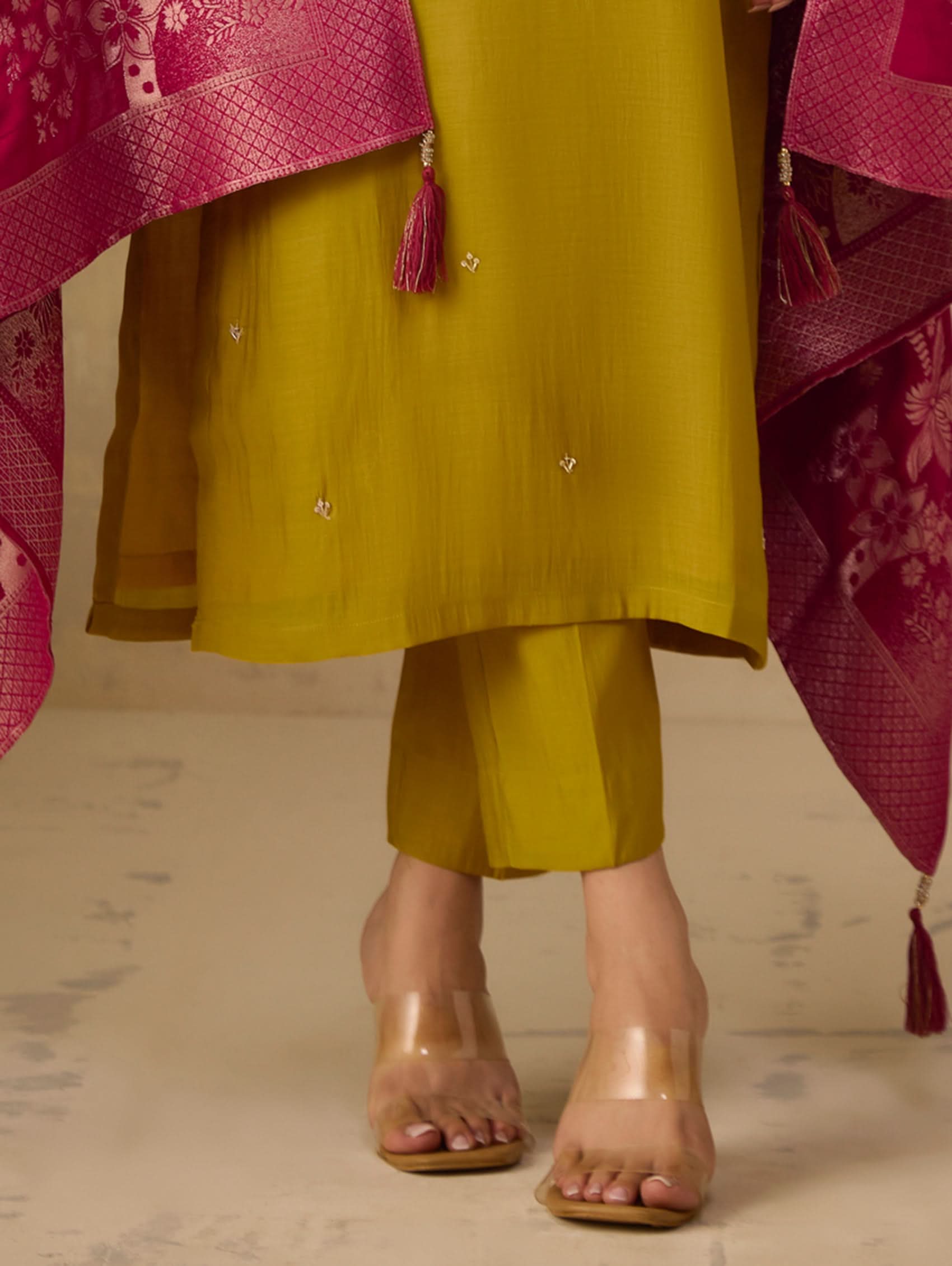 Person wearing a mustard yellow outfit with pink dupatta on a neutral background