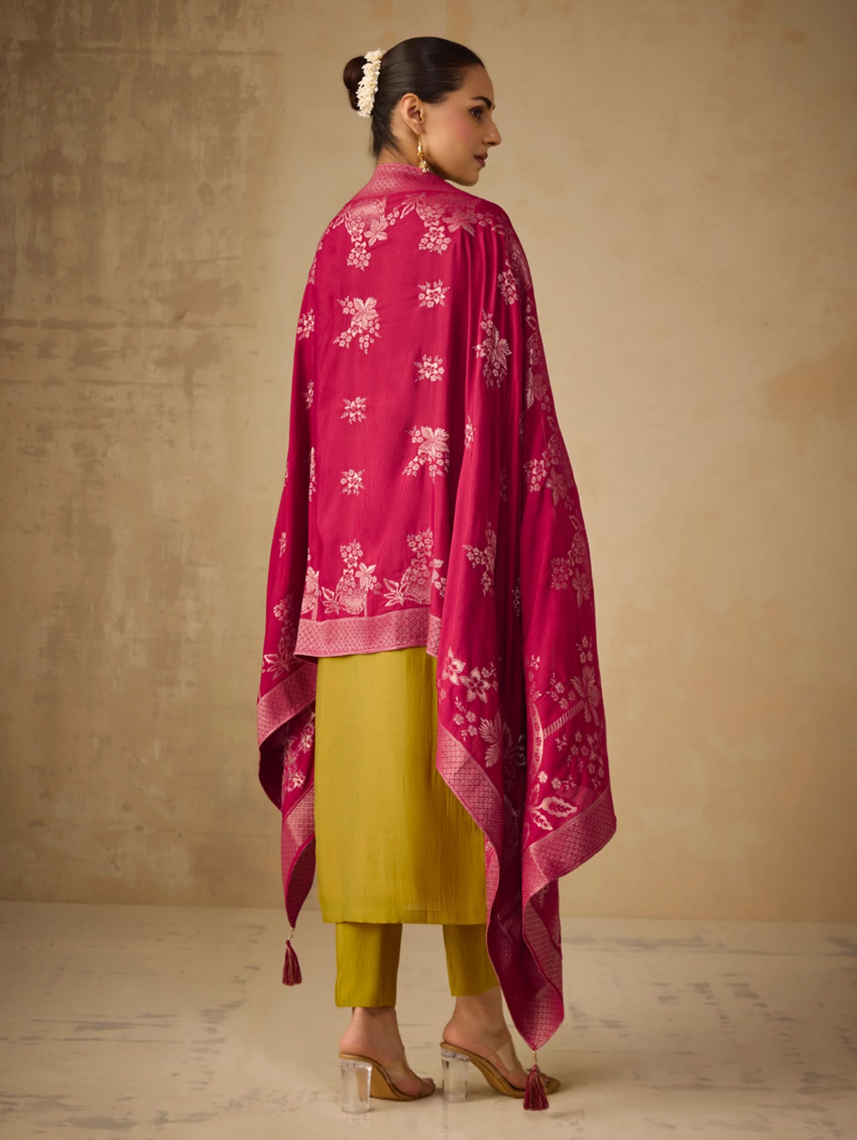 Woman wearing a pink embroidered shawl over a yellow outfit against a beige background
