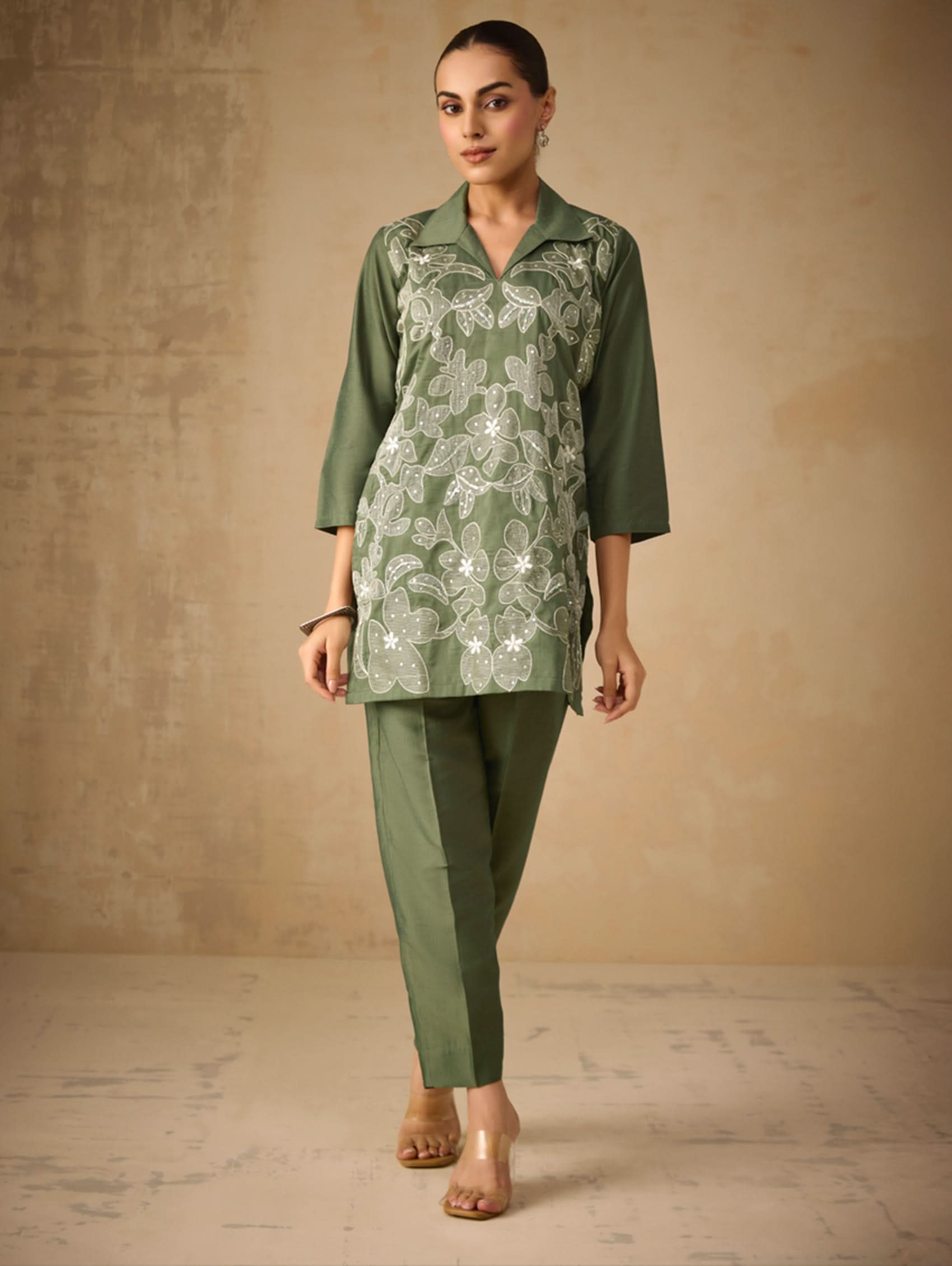 Woman wearing a green floral top and pants against a beige background