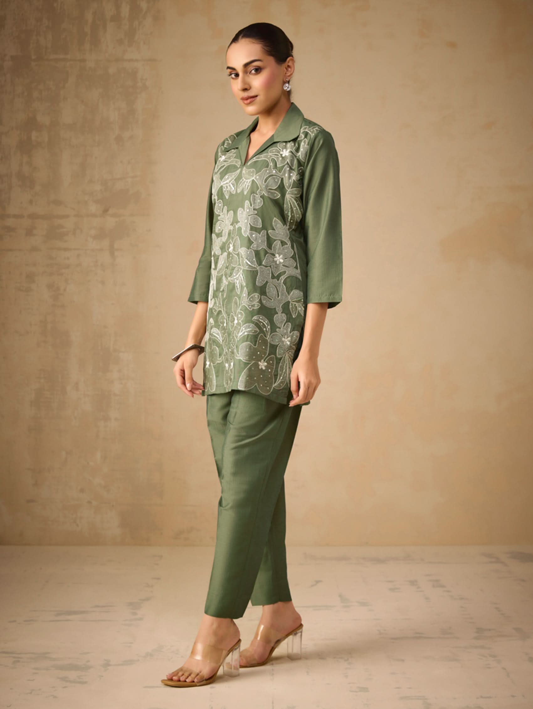 Woman wearing a green floral top and pants against a beige background