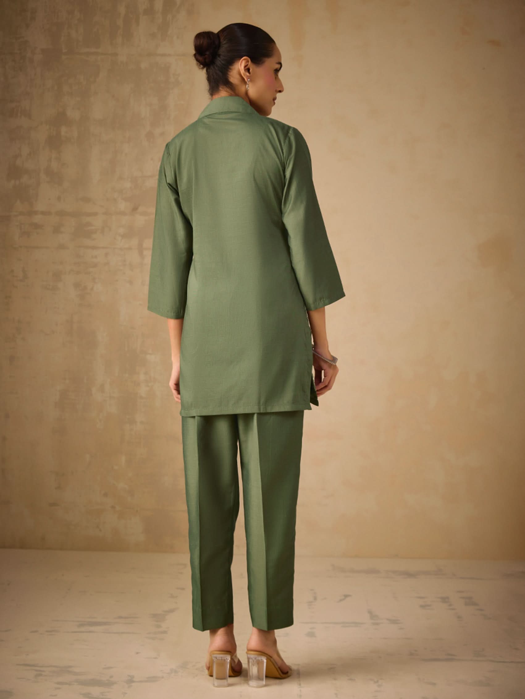 Woman wearing a green outfit standing against a beige wall.