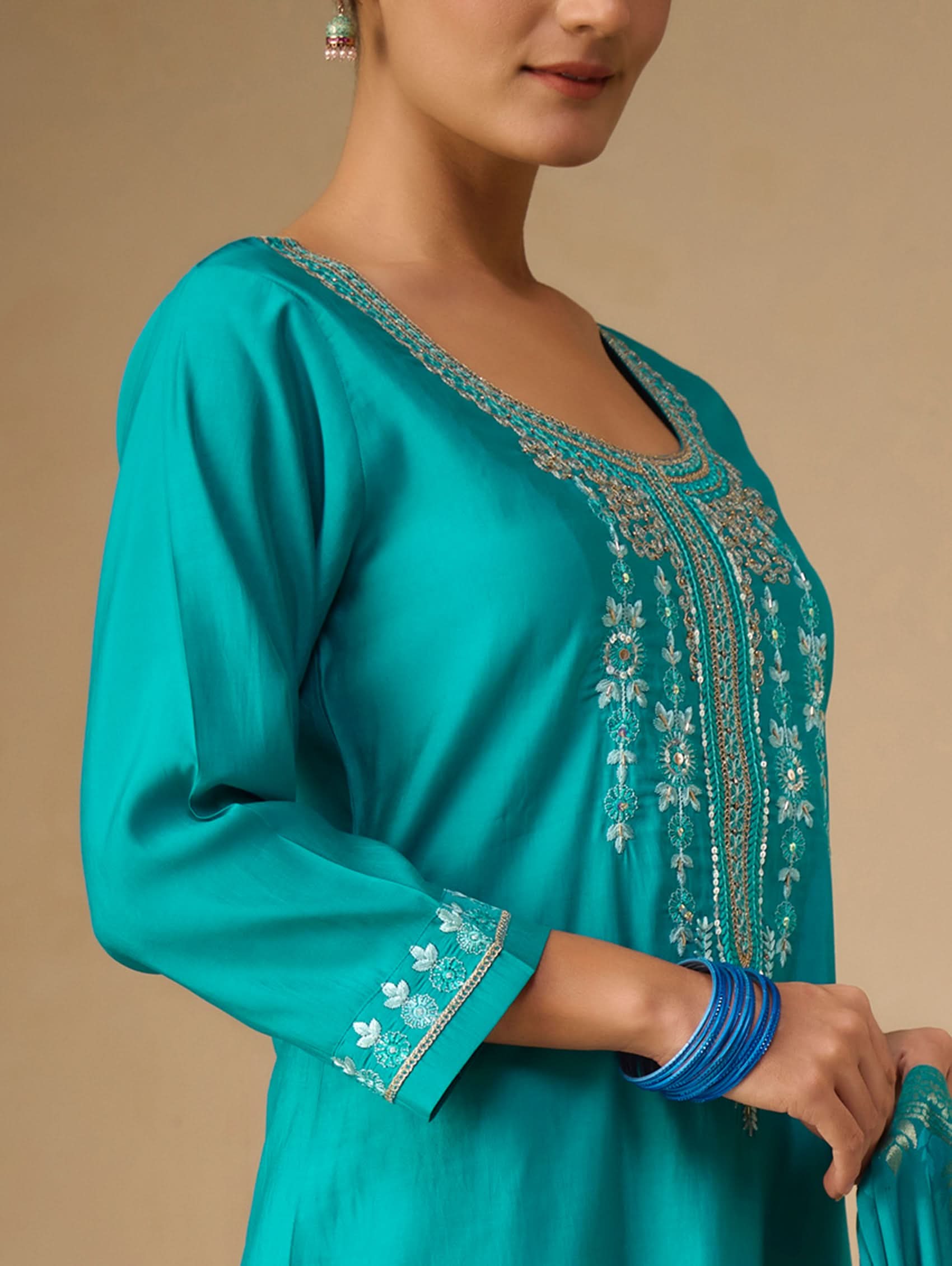 Teal dress with intricate embroidery on a beige background