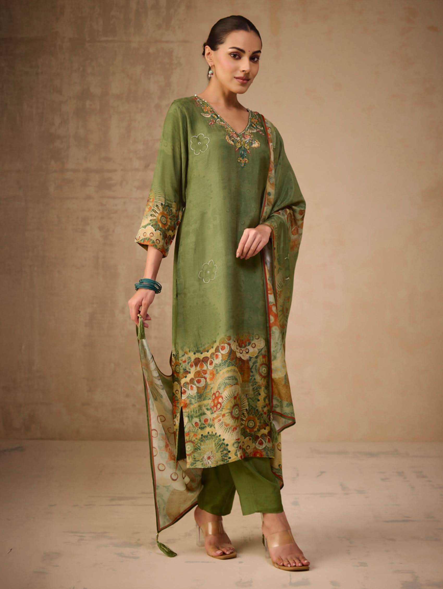 Woman wearing a green traditional outfit with floral patterns against a beige background
