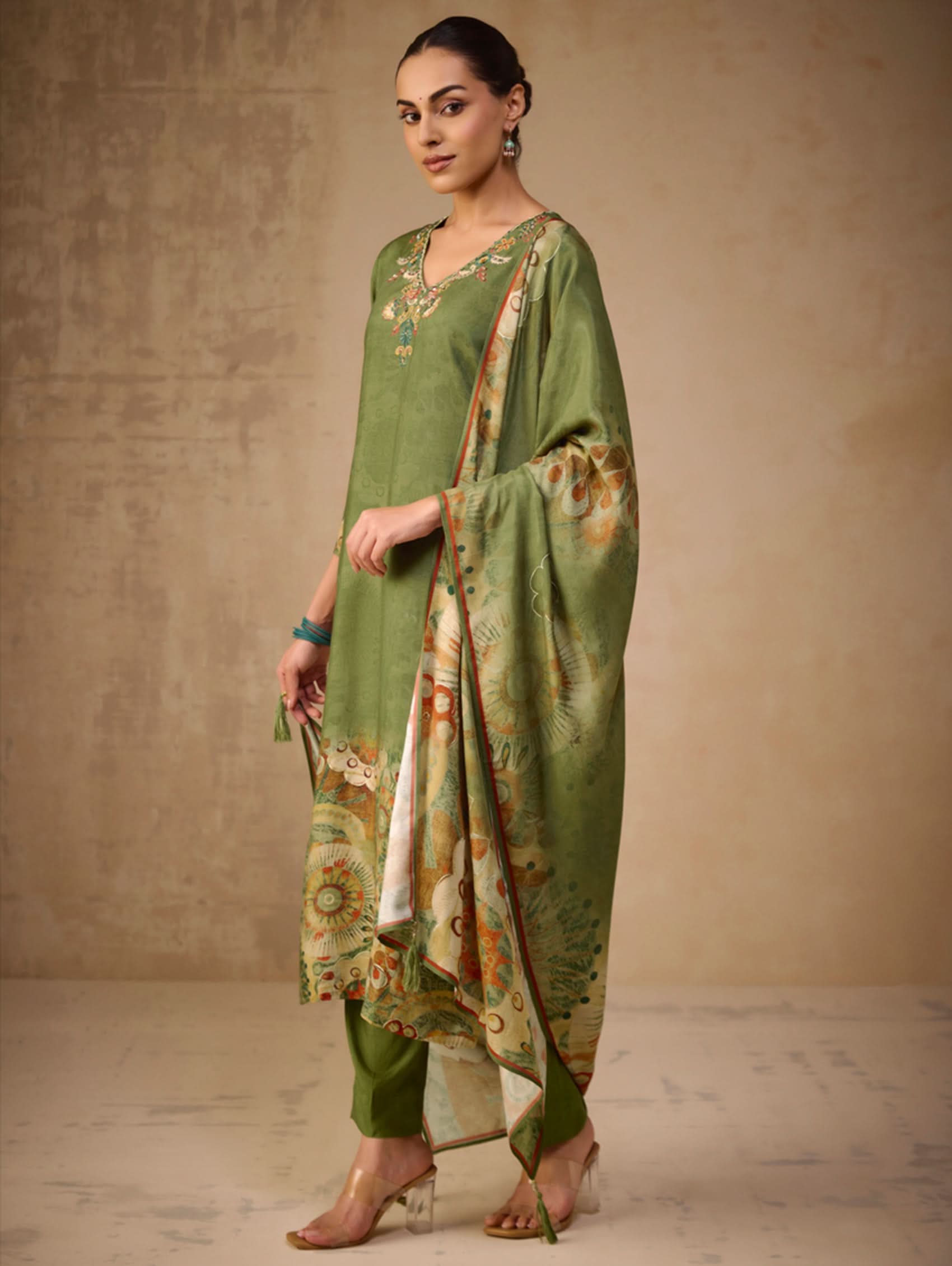 Woman wearing a green traditional outfit with floral patterns against a beige background