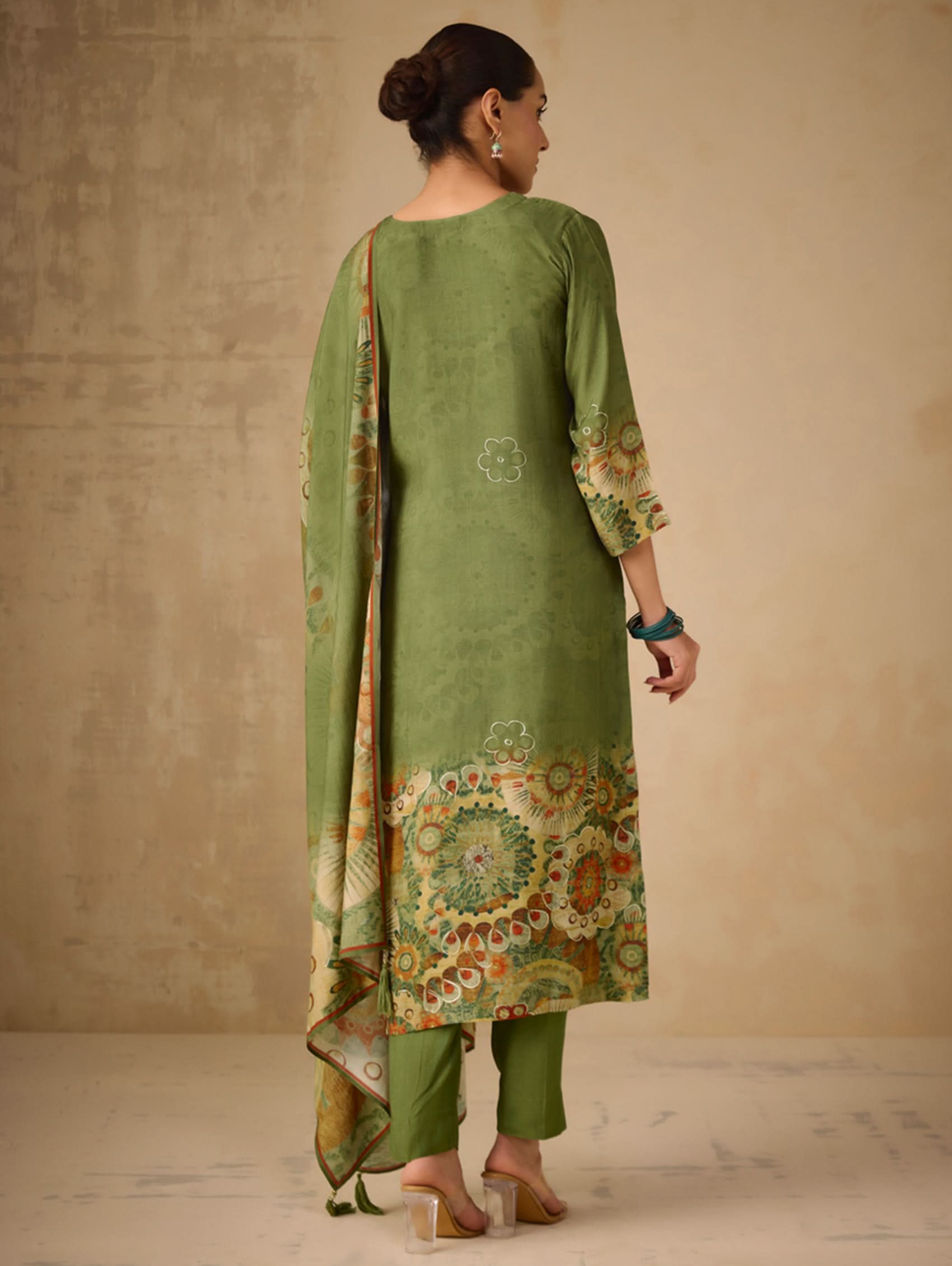 Woman wearing a green traditional outfit with floral patterns on a plain background