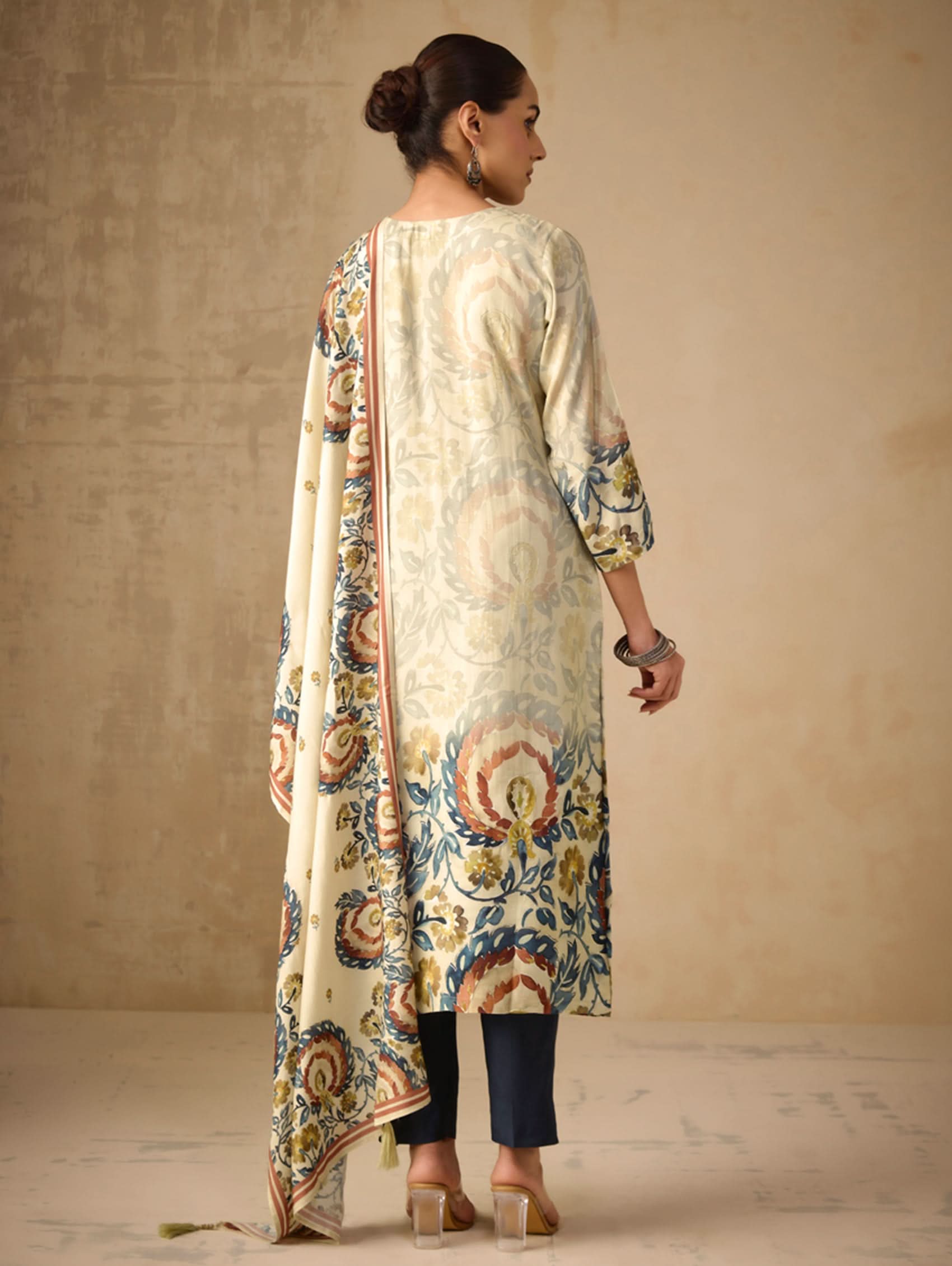 Woman wearing a long, patterned dress with a matching dupatta against a beige background