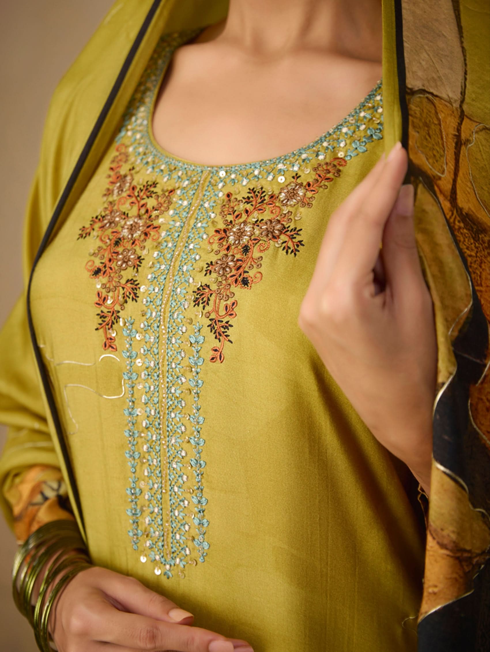 Close-up of a green embroidered garment with floral patterns and beadwork.