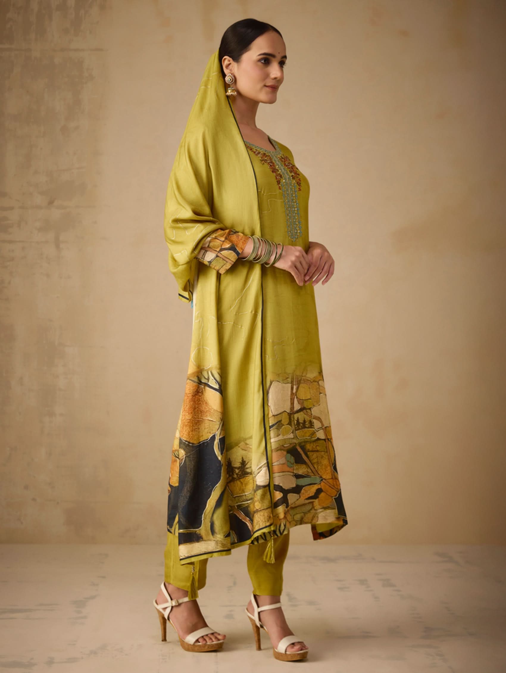 Woman wearing a green traditional outfit with a patterned dupatta against a beige background