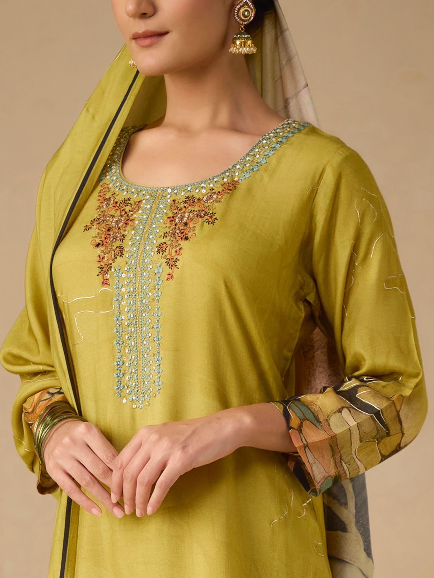 Woman wearing a green embroidered traditional outfit with a beige background