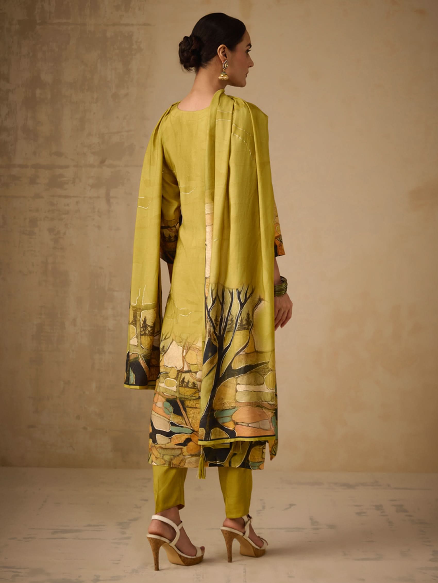 Woman wearing a green traditional outfit with a patterned shawl against a beige background