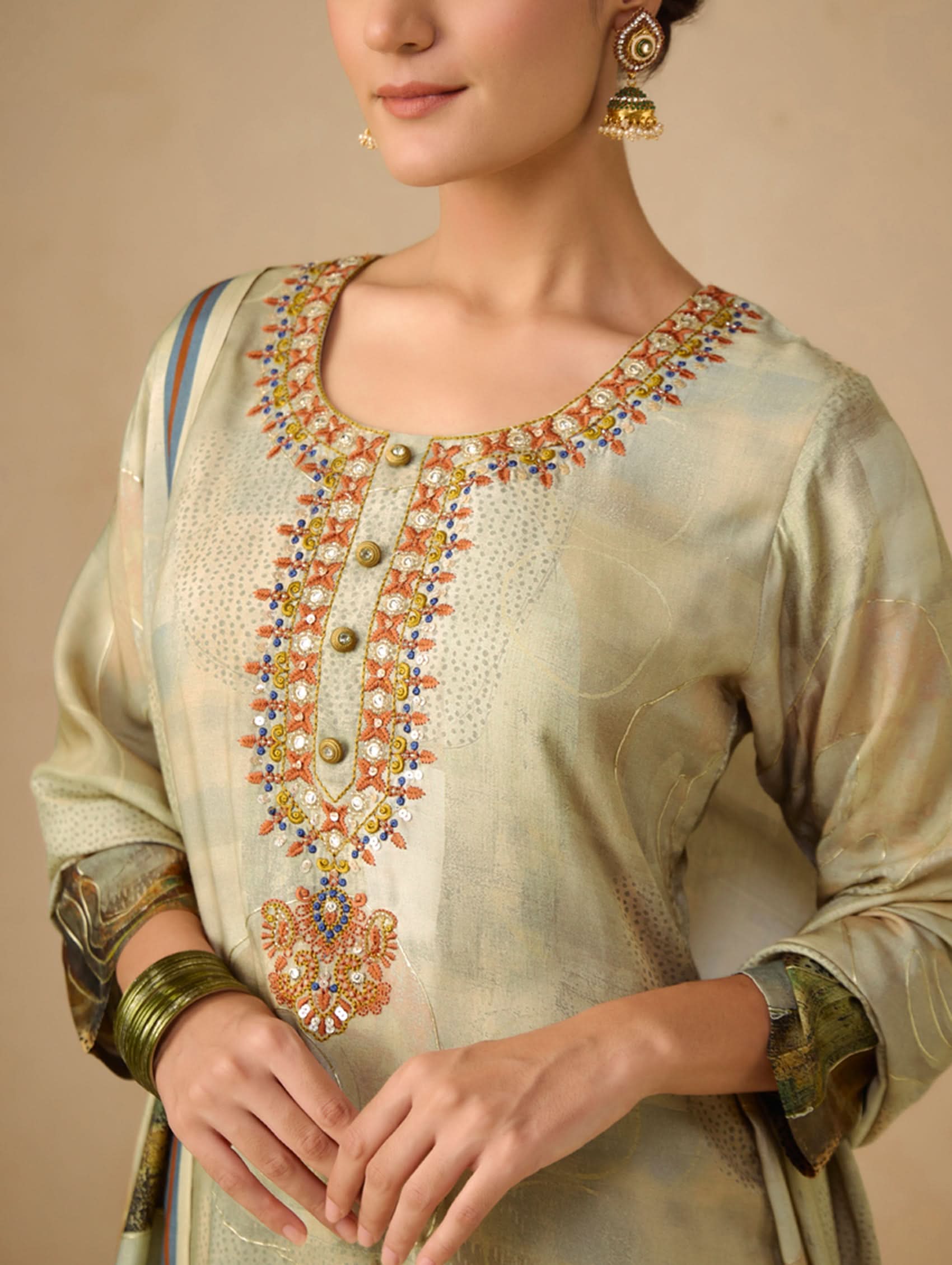 Woman wearing a traditional embroidered outfit with gold jewelry on a beige background