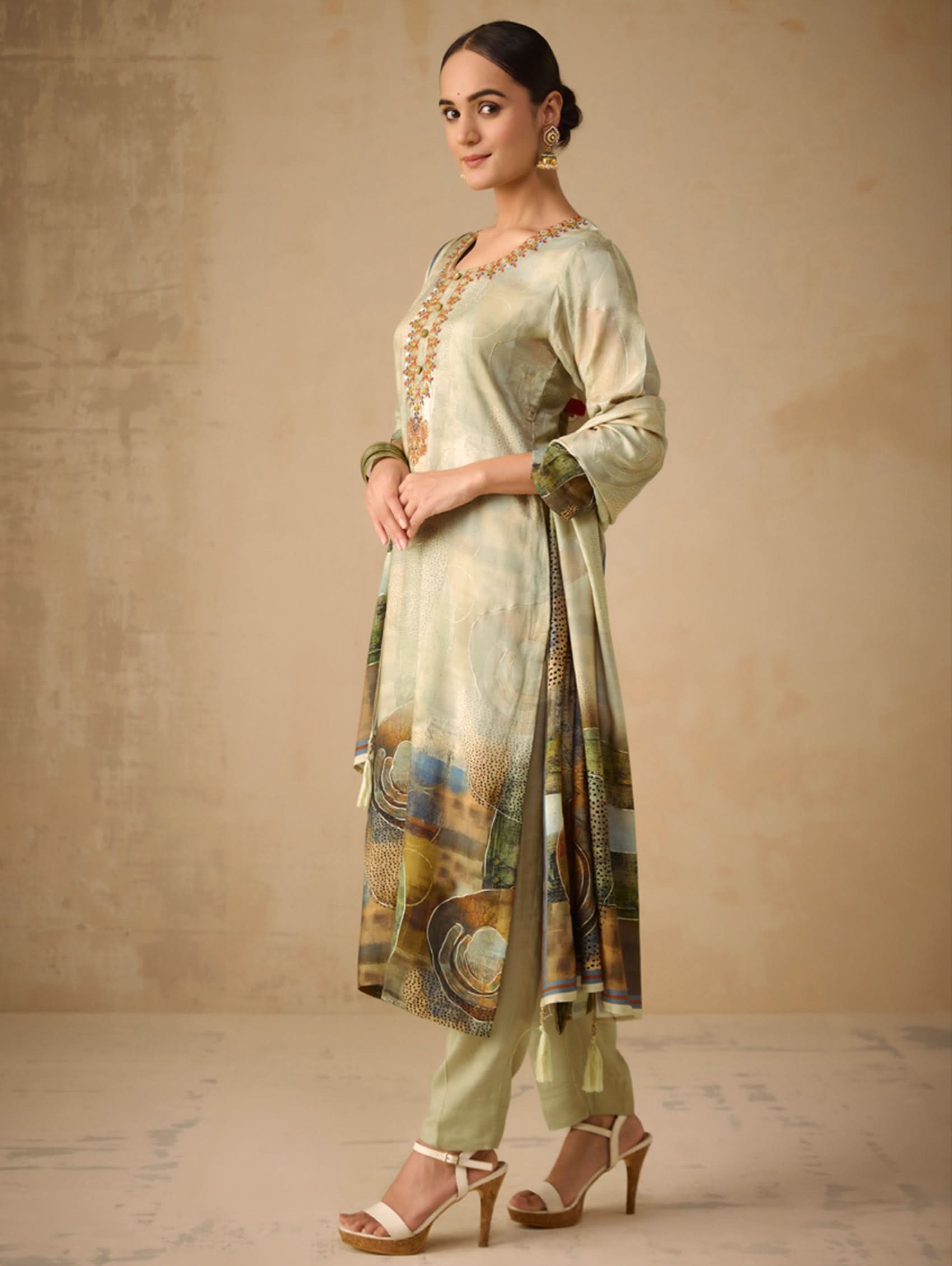 Woman wearing a light green traditional outfit with a patterned scarf against a beige background